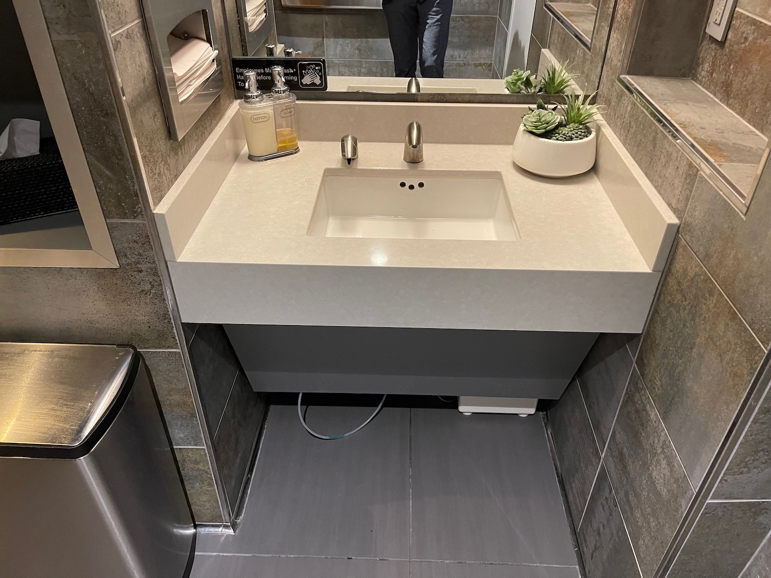 a bathroom sink with a mirror and a person standing in the background