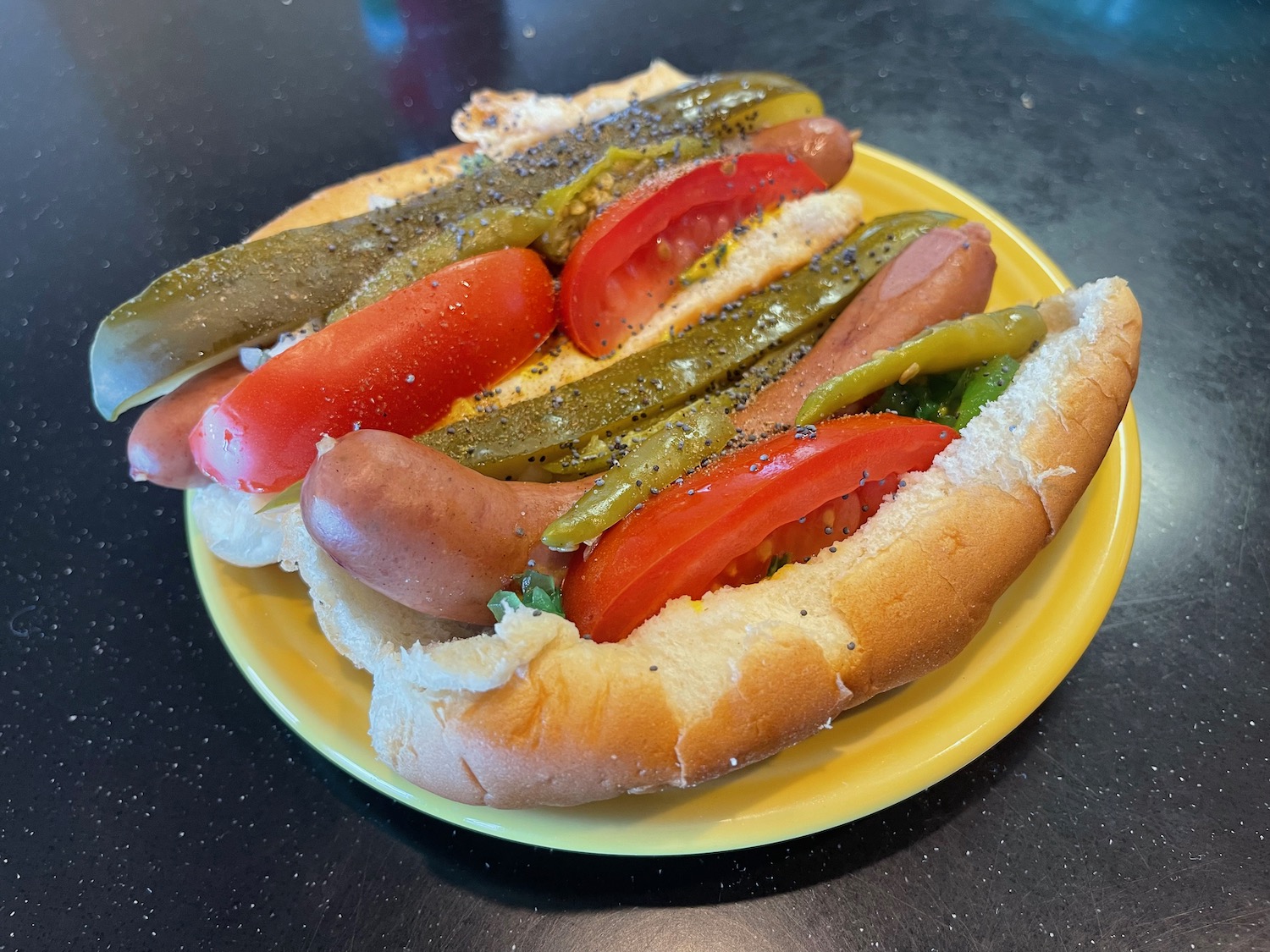 a hot dog with tomatoes and pickles on a yellow plate