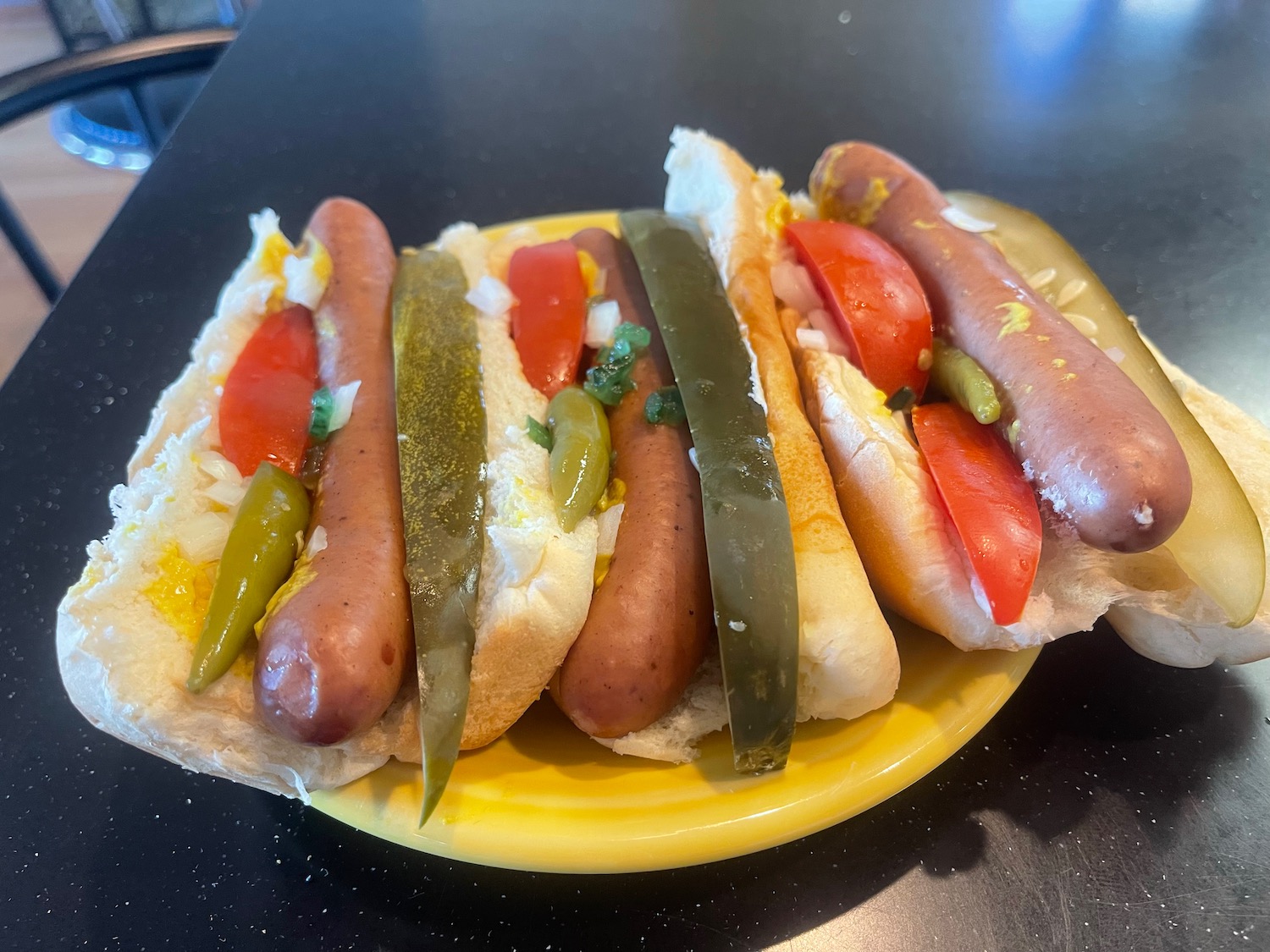 a plate of hot dogs with pickles and tomatoes