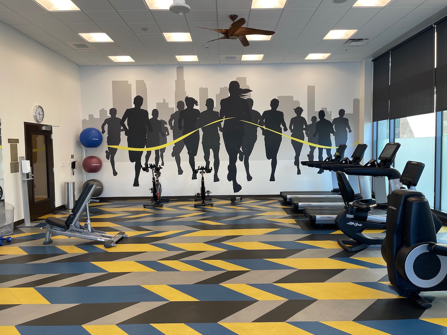 a room with exercise equipment and a wall mural of people running