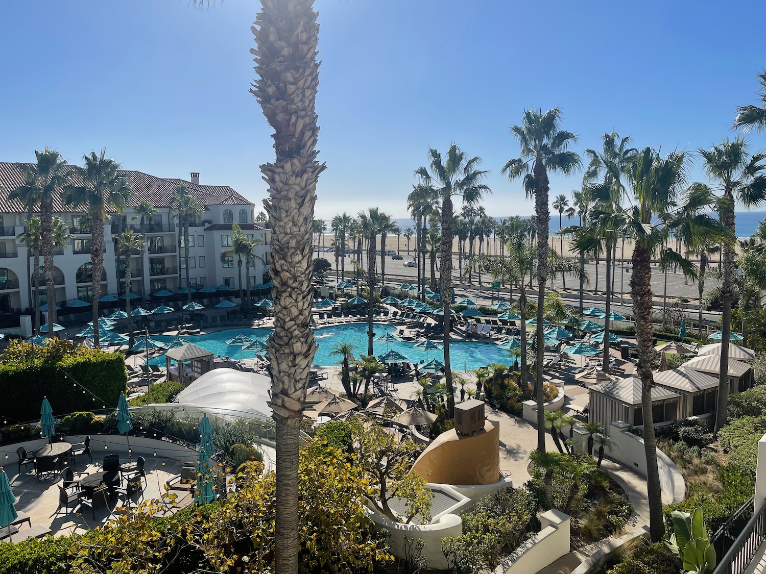 a pool with palm trees and a building with a beach and blue sky