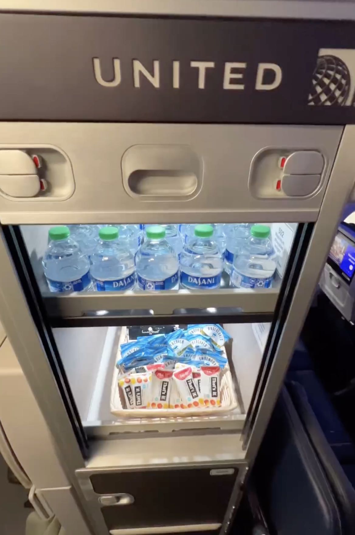 a refrigerator with bottles of water and a tray of candy