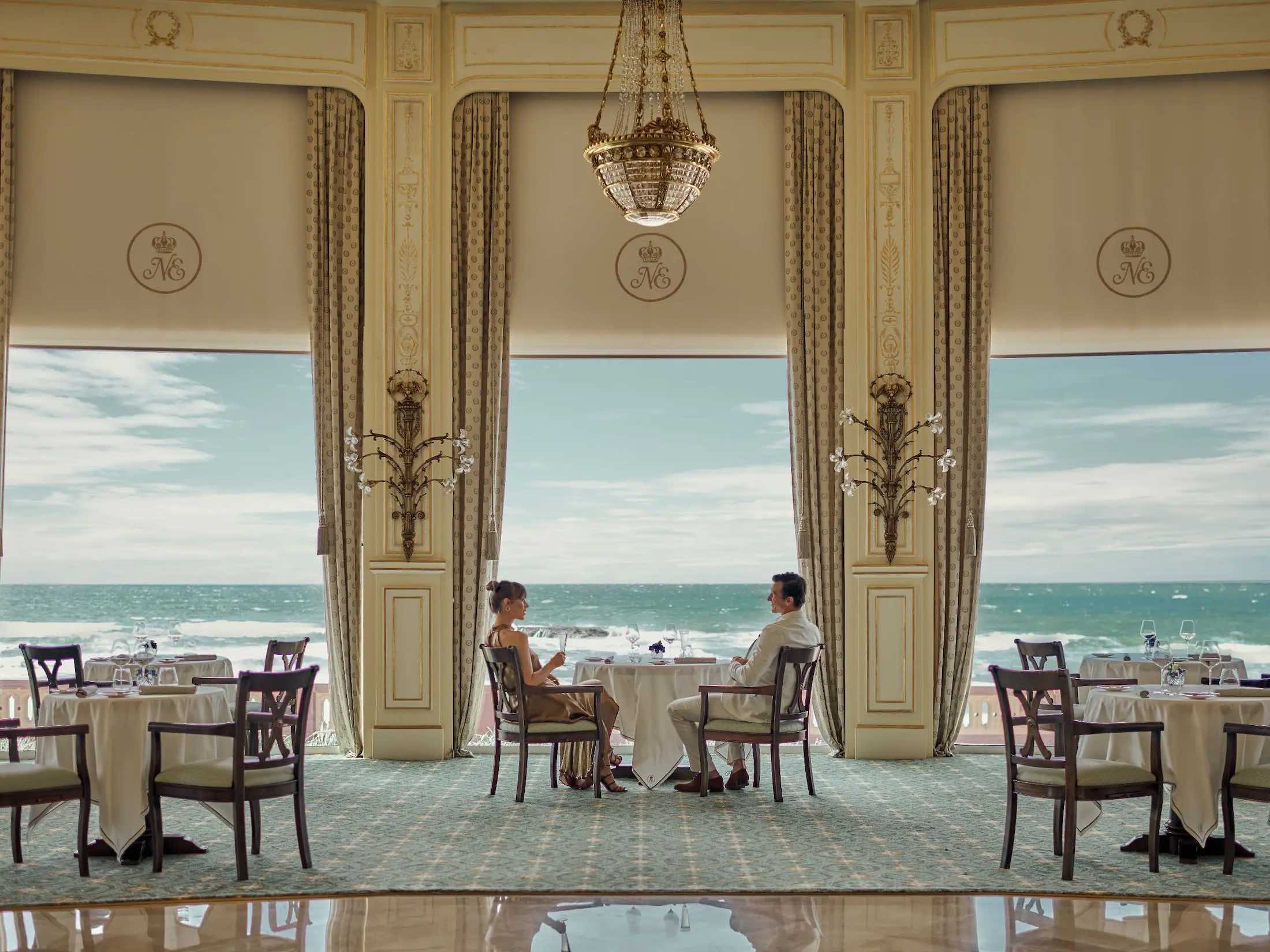 a man and woman sitting at tables in a room with ocean view
