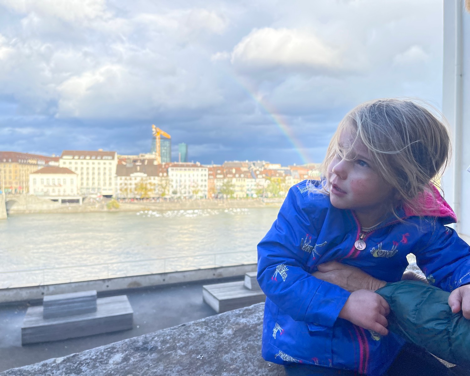 a girl sitting on a ledge looking at a rainbow