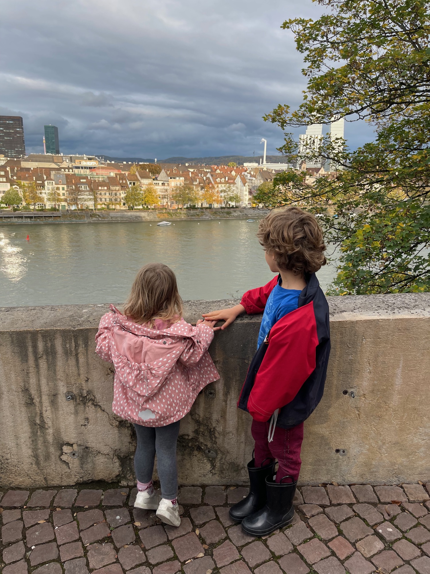 a boy and girl standing on a concrete wall looking at a body of water