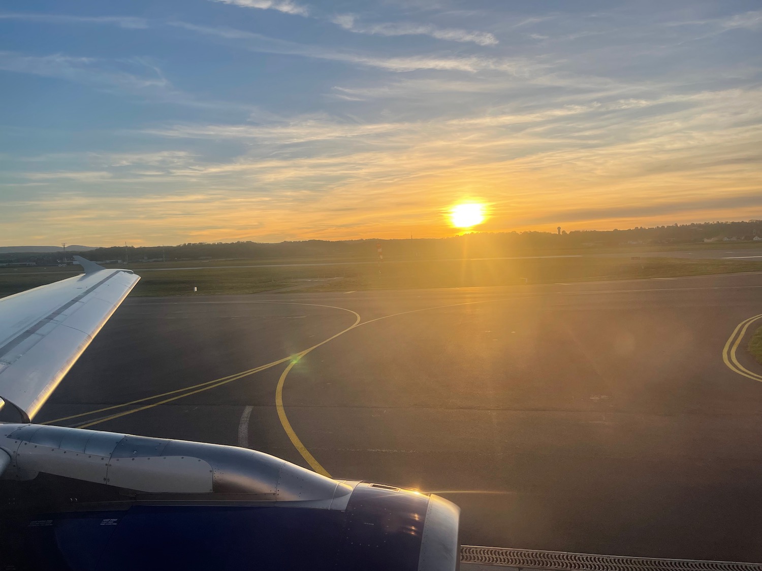 an airplane wing on a runway with the sun setting in the background