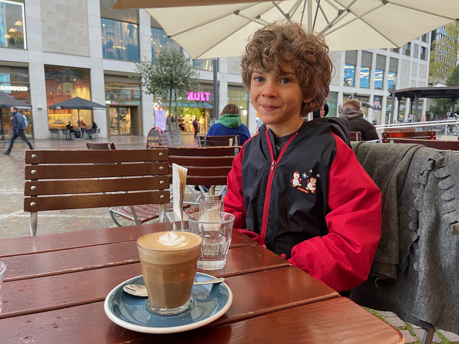 a boy sitting at a table with a cup of coffee