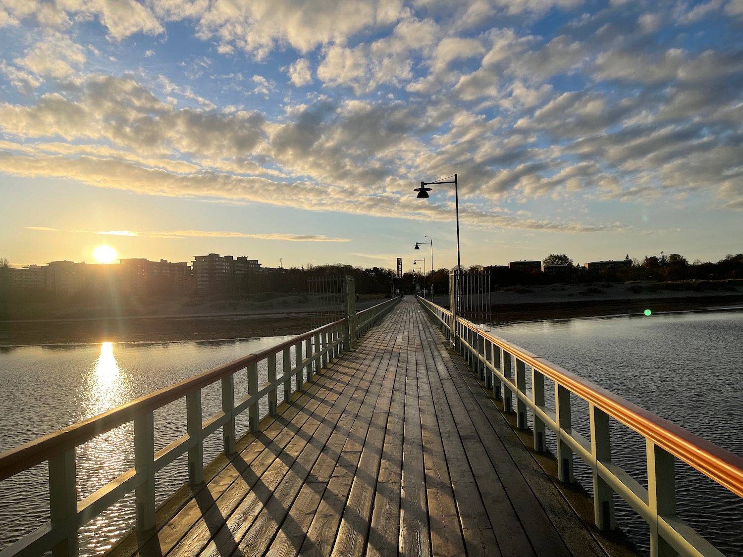 a wooden bridge over water with a body of water and a city in the background