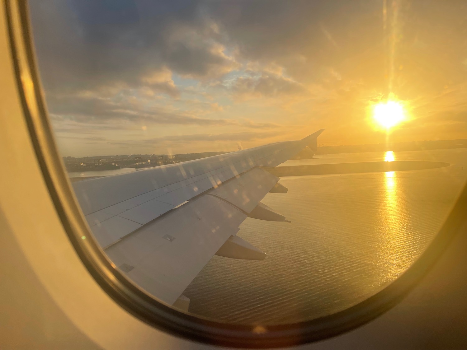 an airplane wing over water and the sun