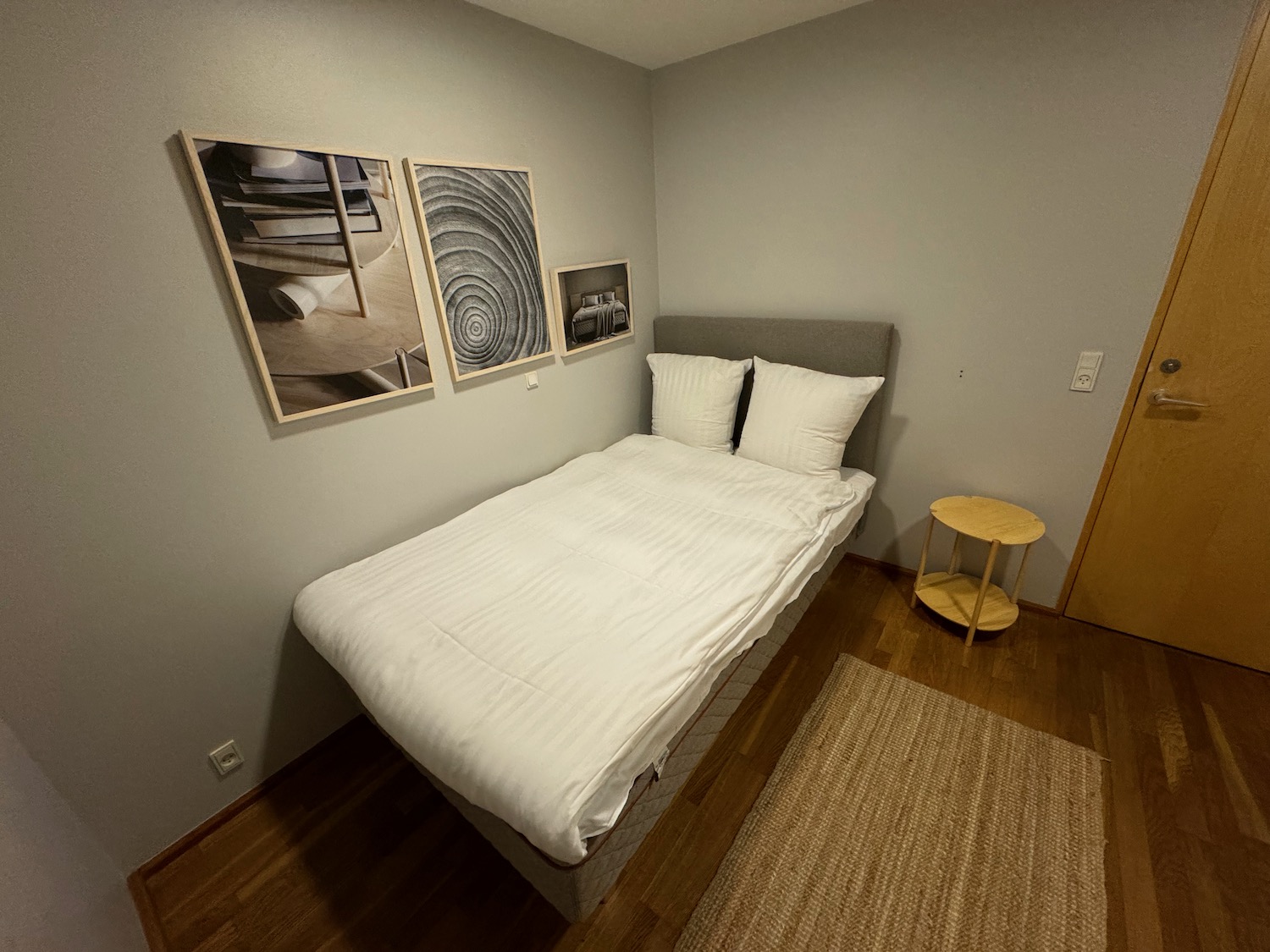 a bed with white sheets and pillows in a room with a wood floor