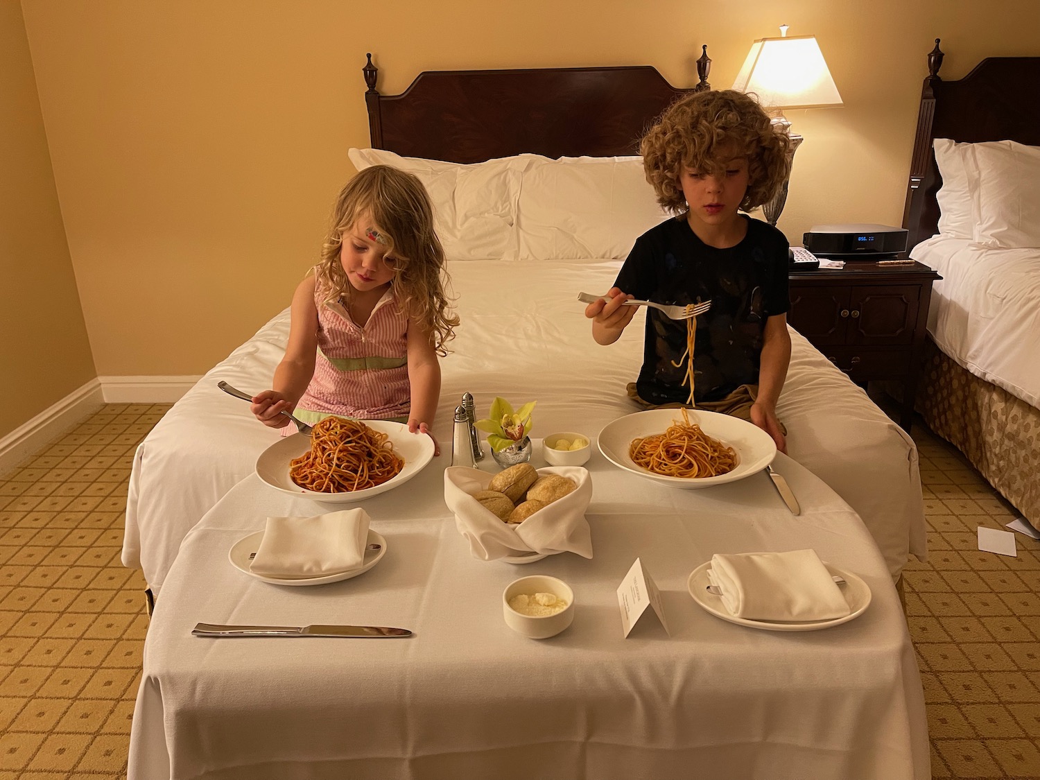 a couple of kids eating spaghetti on a bed