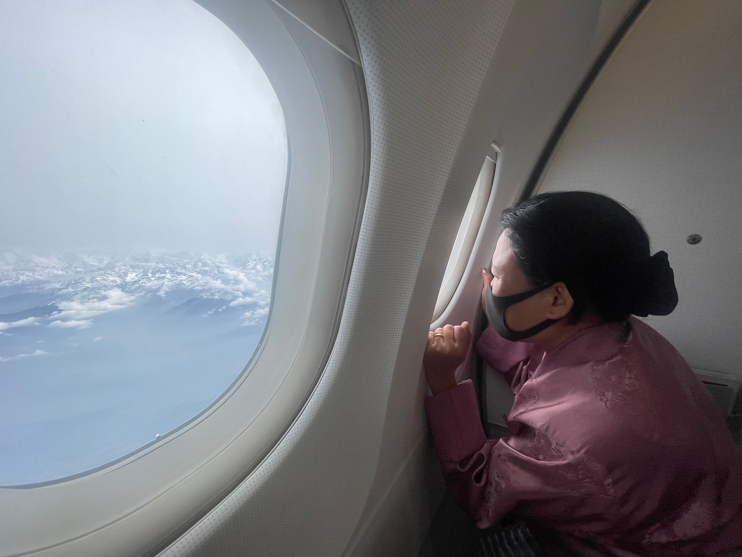 a woman wearing a mask looking out of an airplane window