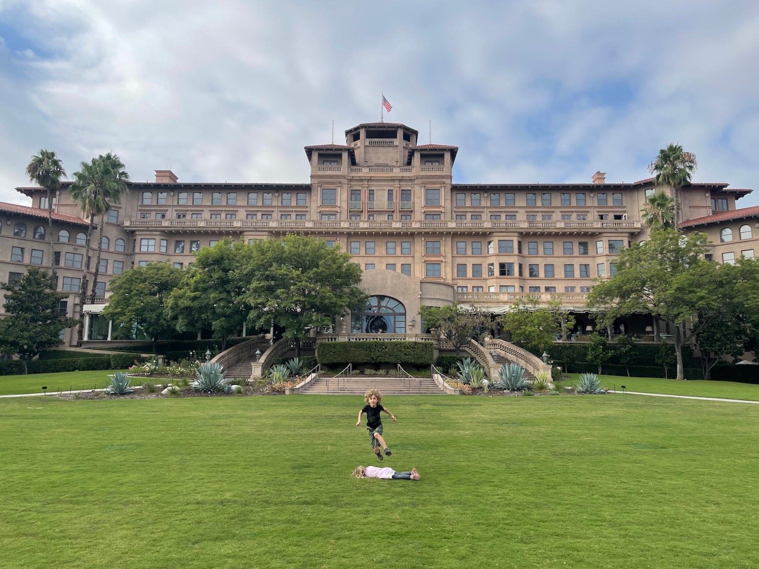 a boy jumping in the grass in front of a large building