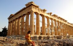 a woman sitting on a rock in front of a large building