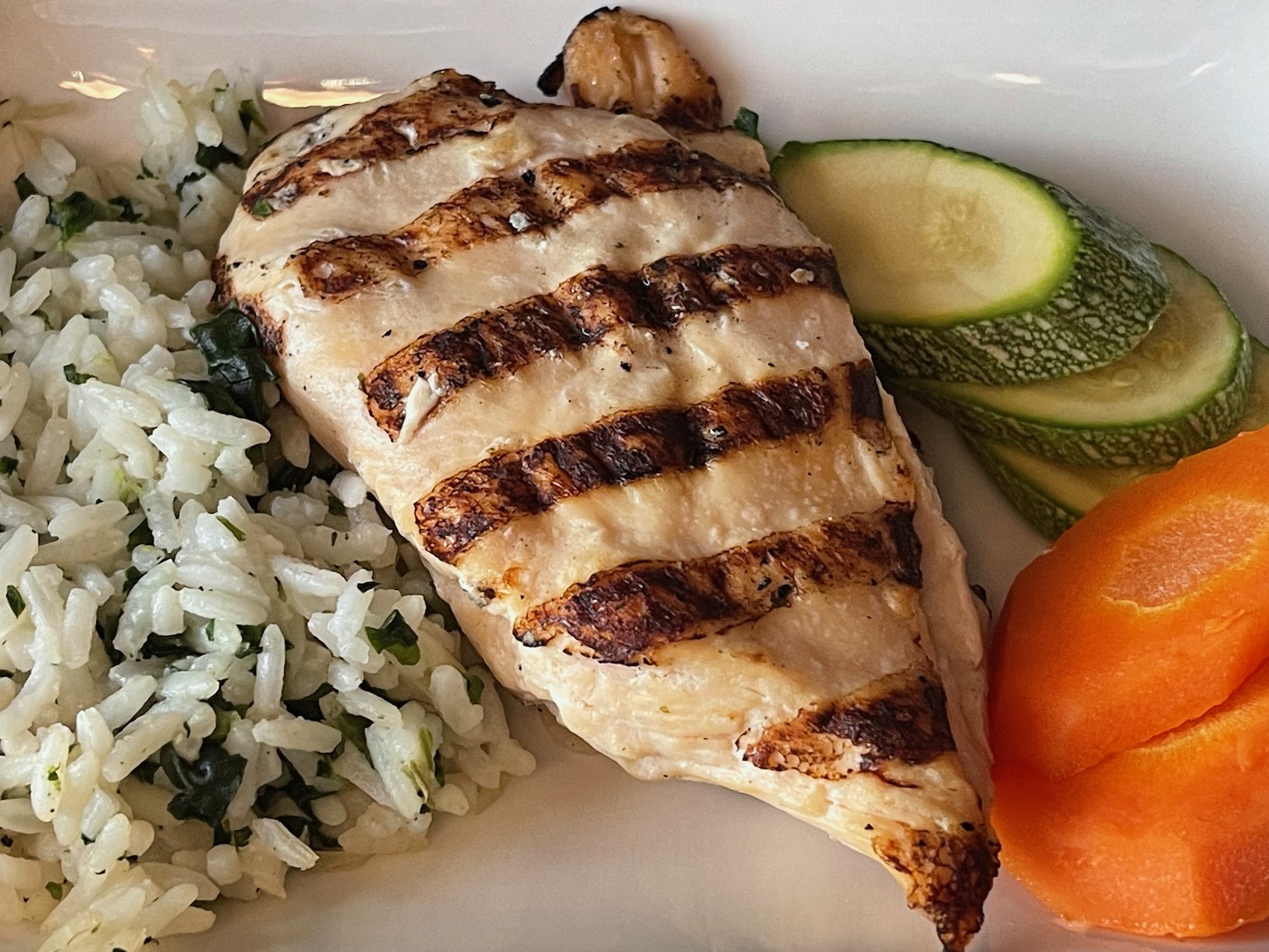 a plate of food with a grilled chicken breast and rice and vegetables