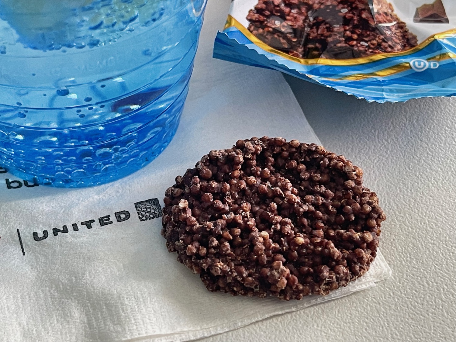 a chocolate chip cookie on a napkin next to a plastic cup of water