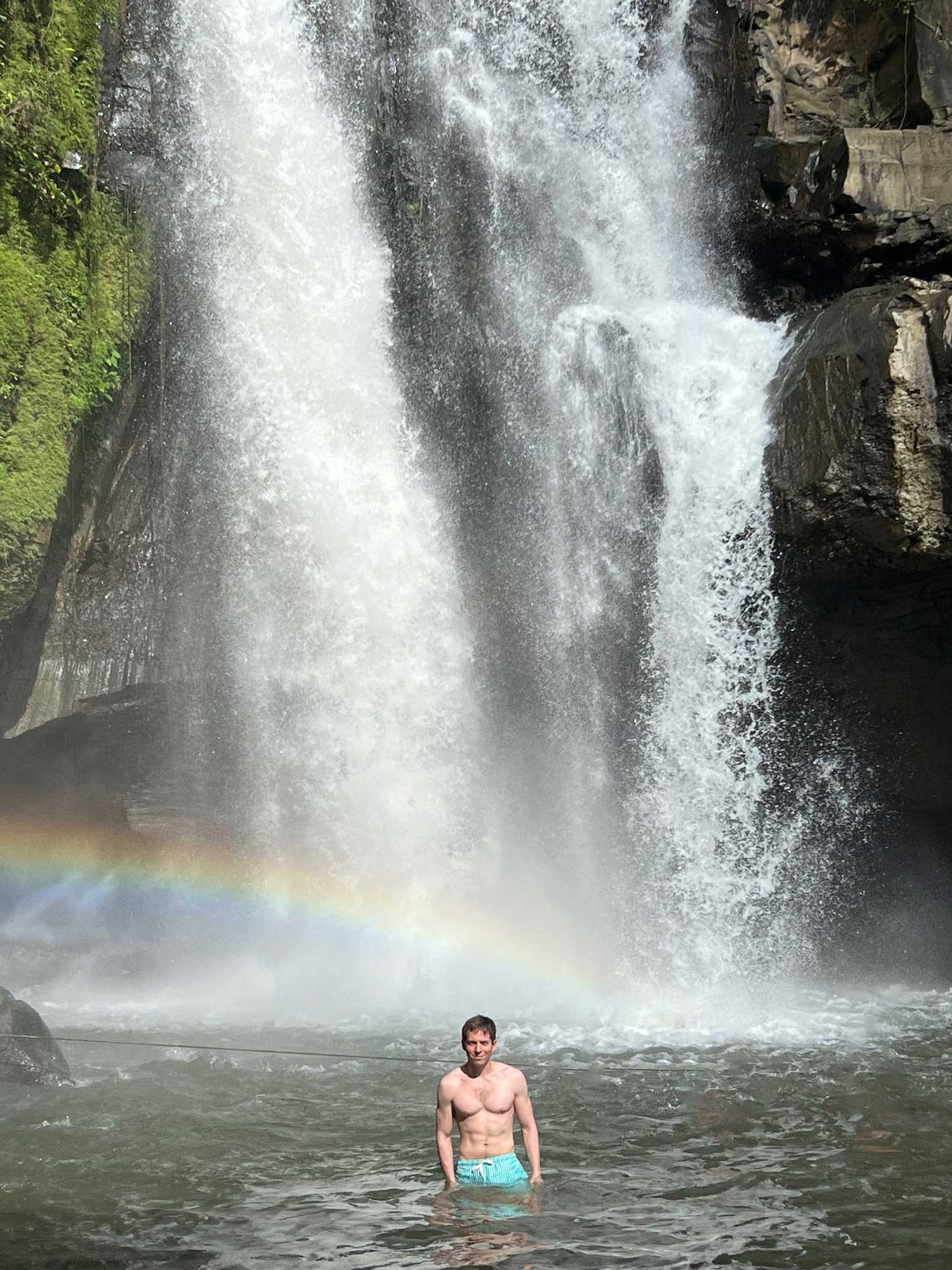 a man standing in a river with a rainbow in the background