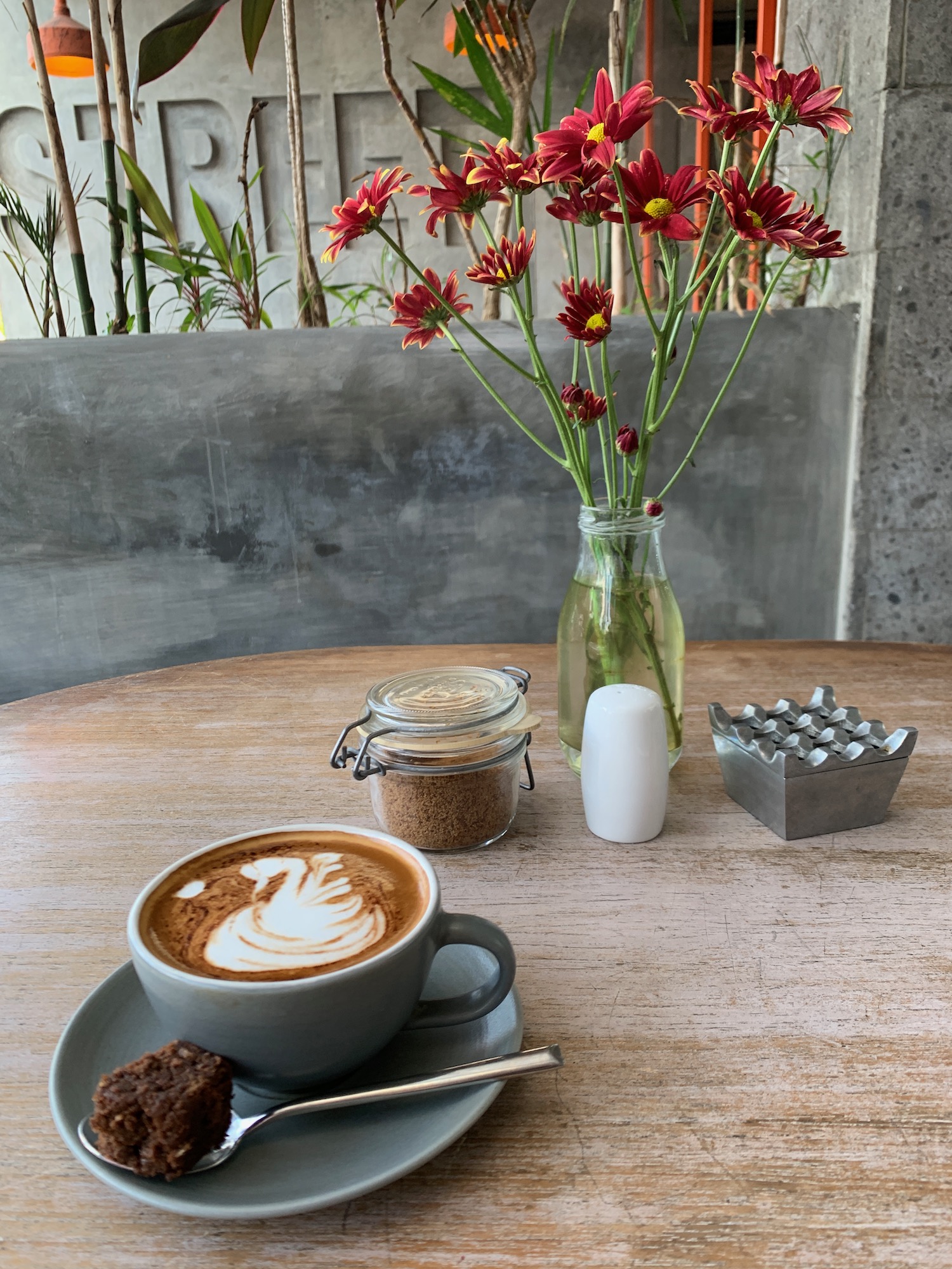 a cup of coffee and brownie on a table with red flowers