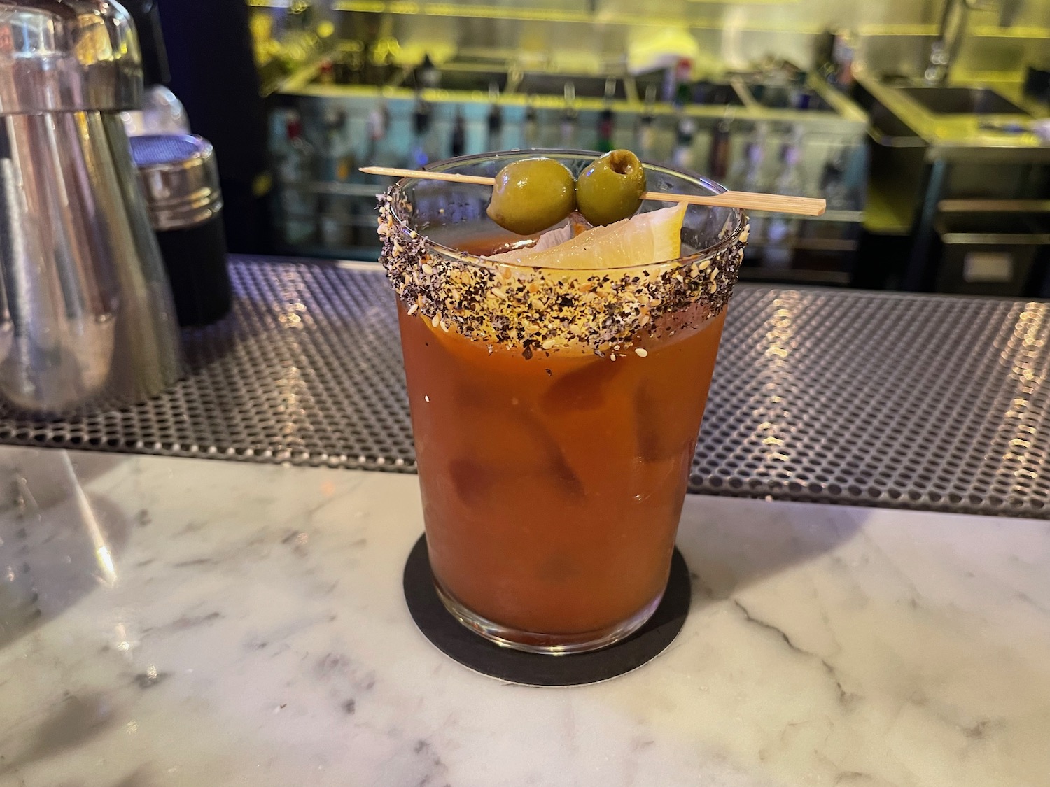 a glass of liquid with a garnish and olives