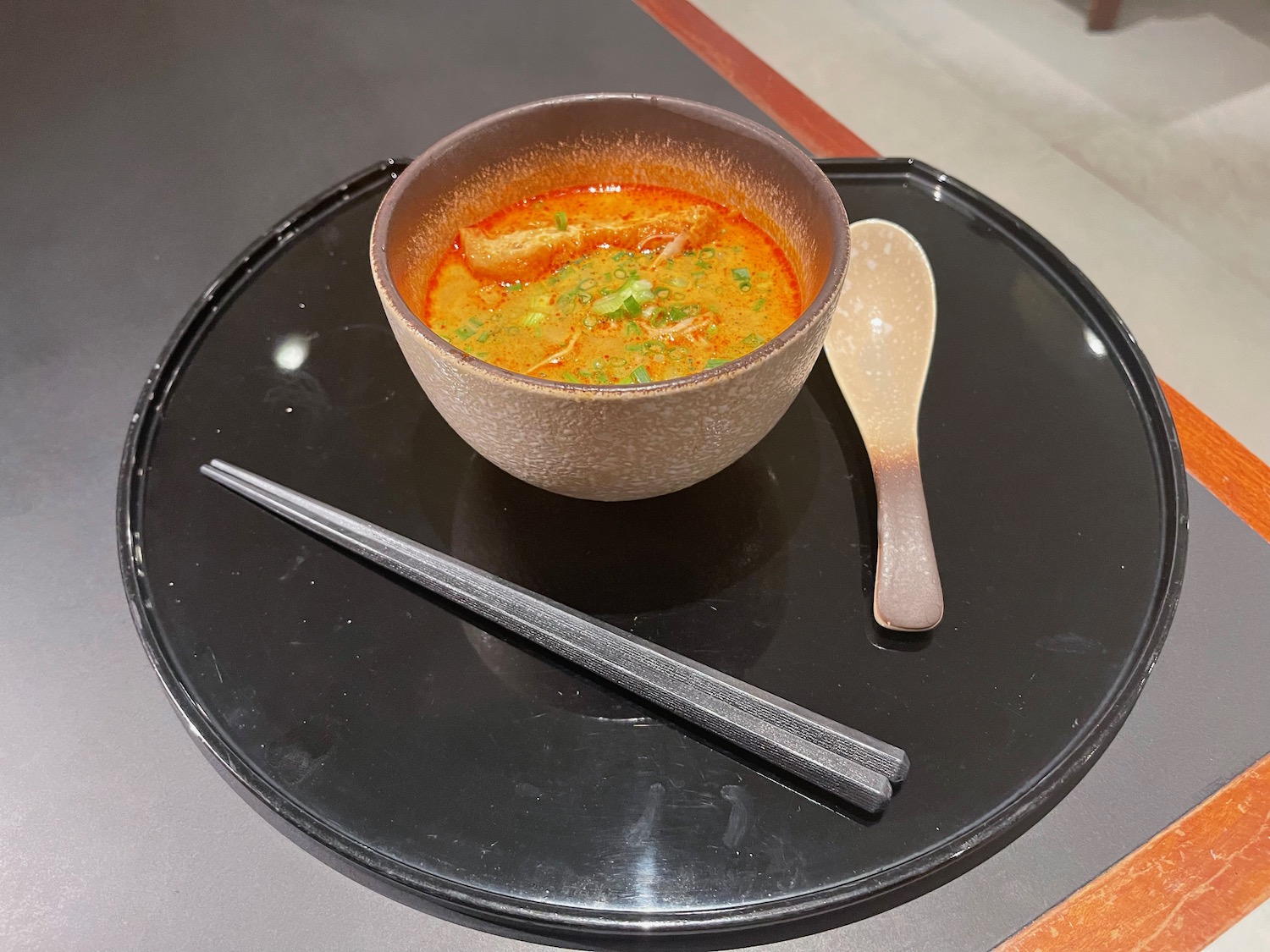 a bowl of soup and chopsticks on a black tray