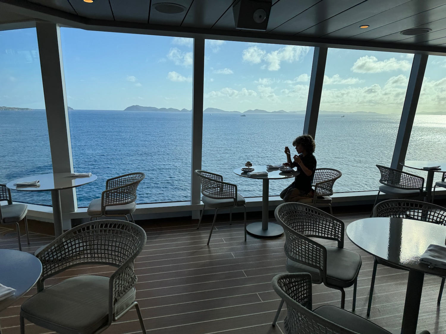 a person sitting at a table with chairs and a large window overlooking the ocean