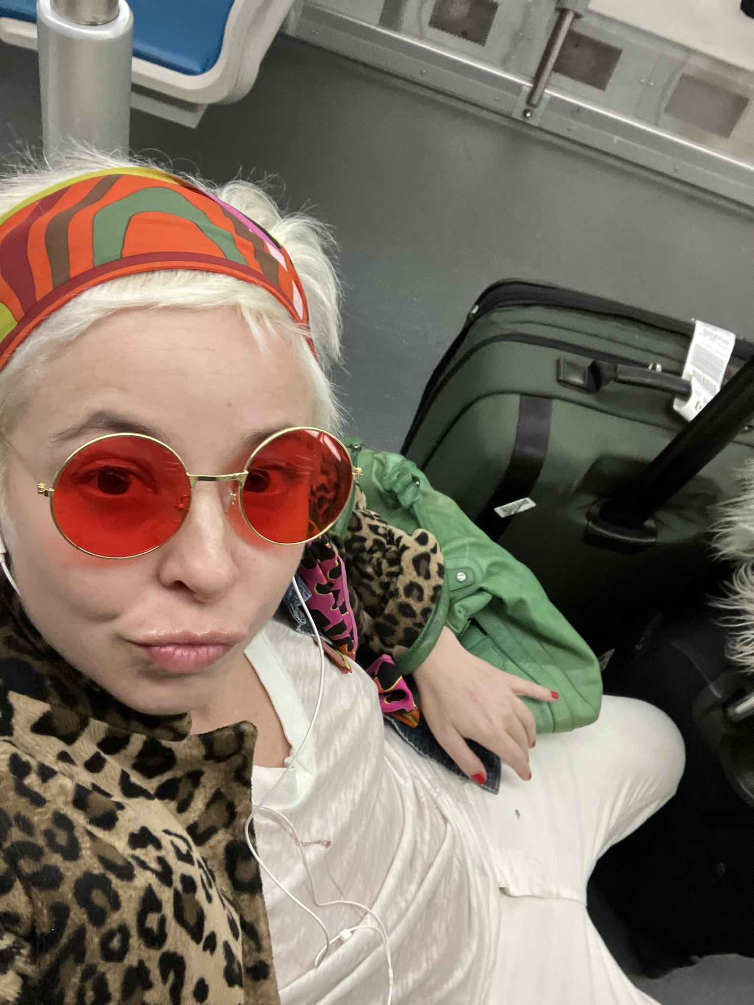 a woman wearing red sunglasses and a headband sitting on a luggage