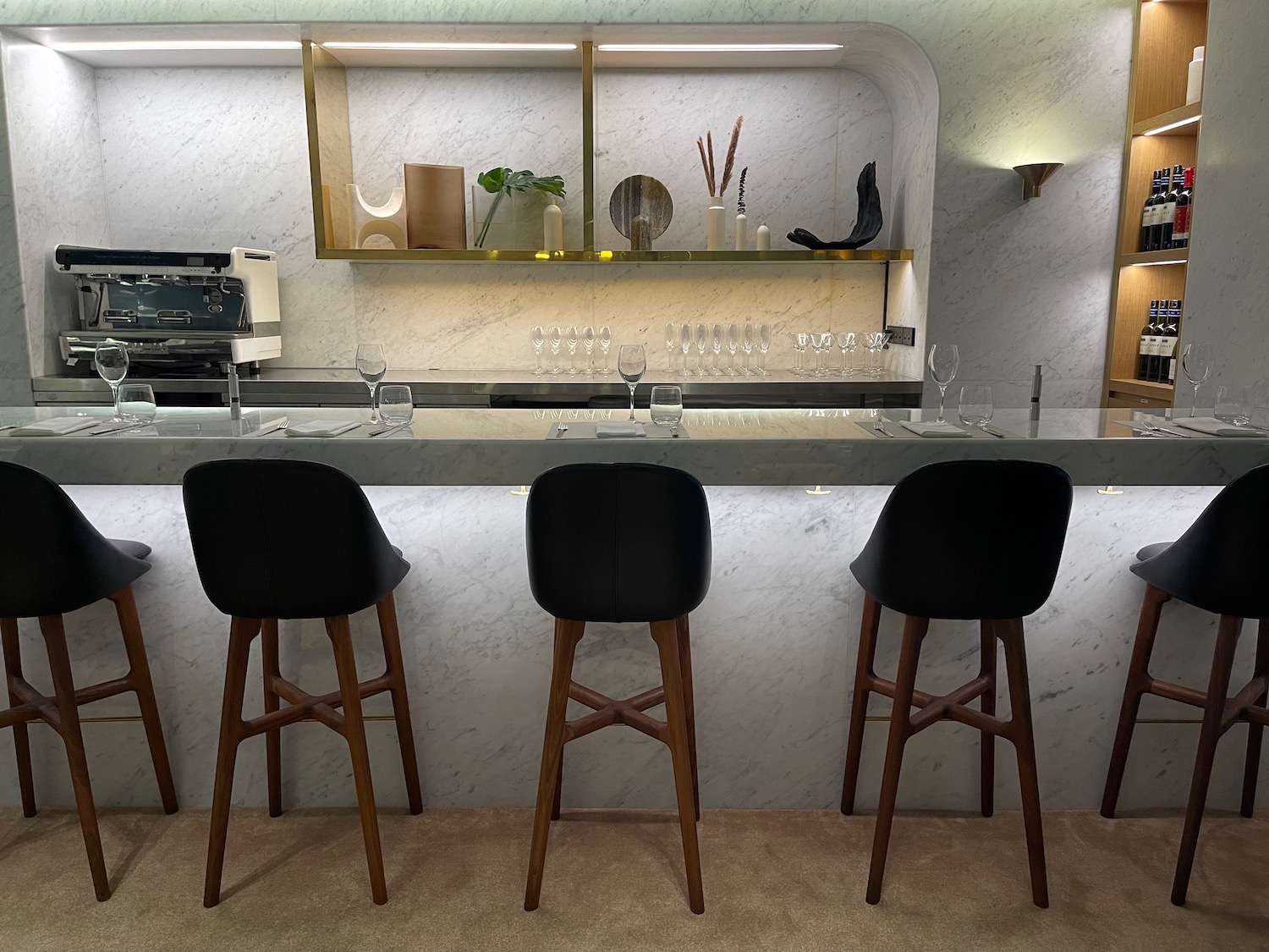 a bar with black chairs and a shelf with wine glasses