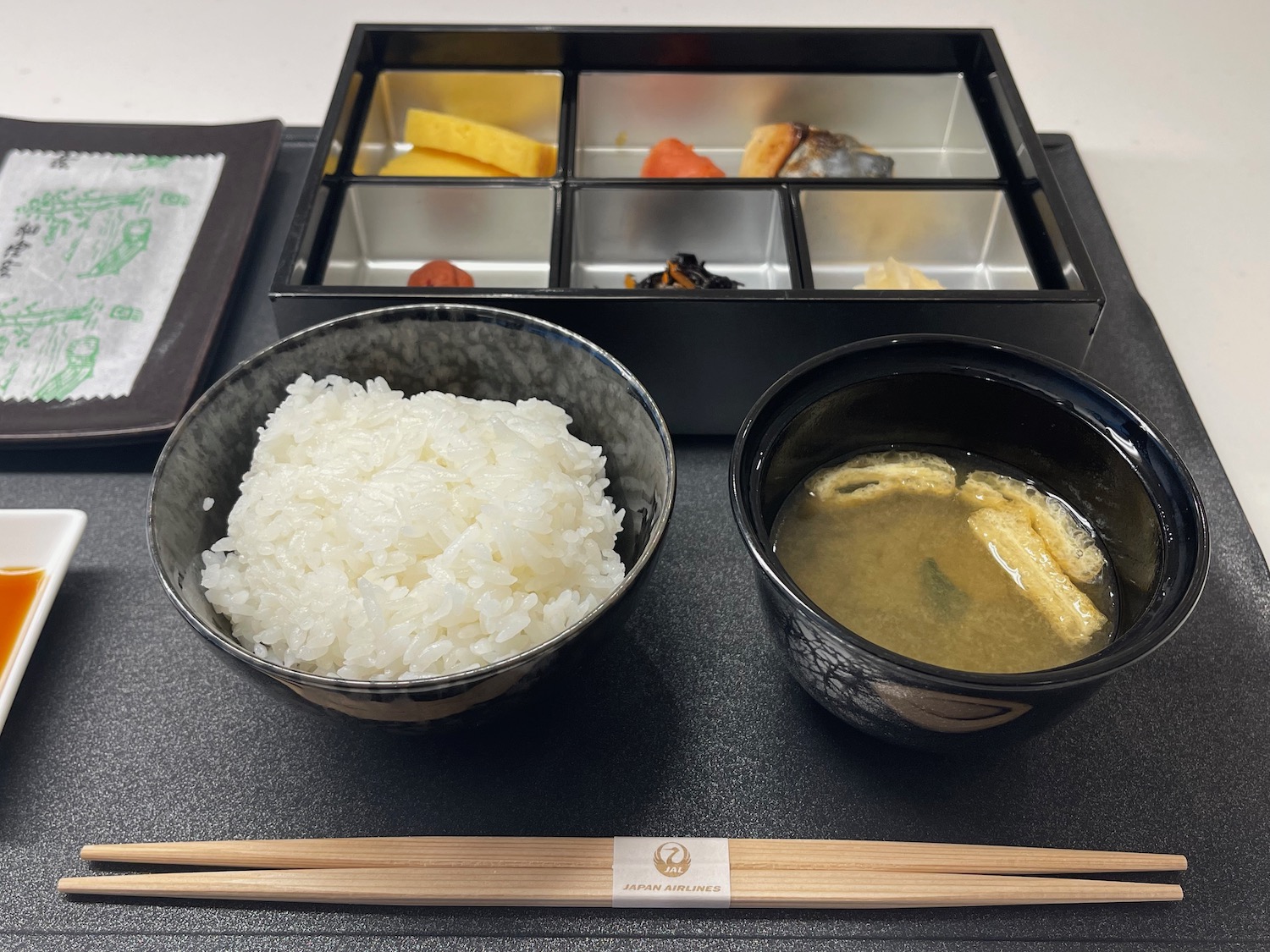 a bowl of rice and soup next to a tray of food