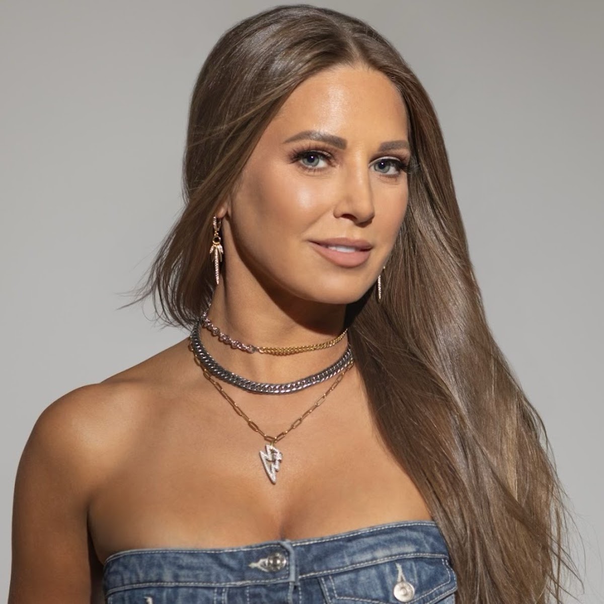 a woman with long hair wearing a denim dress and necklaces