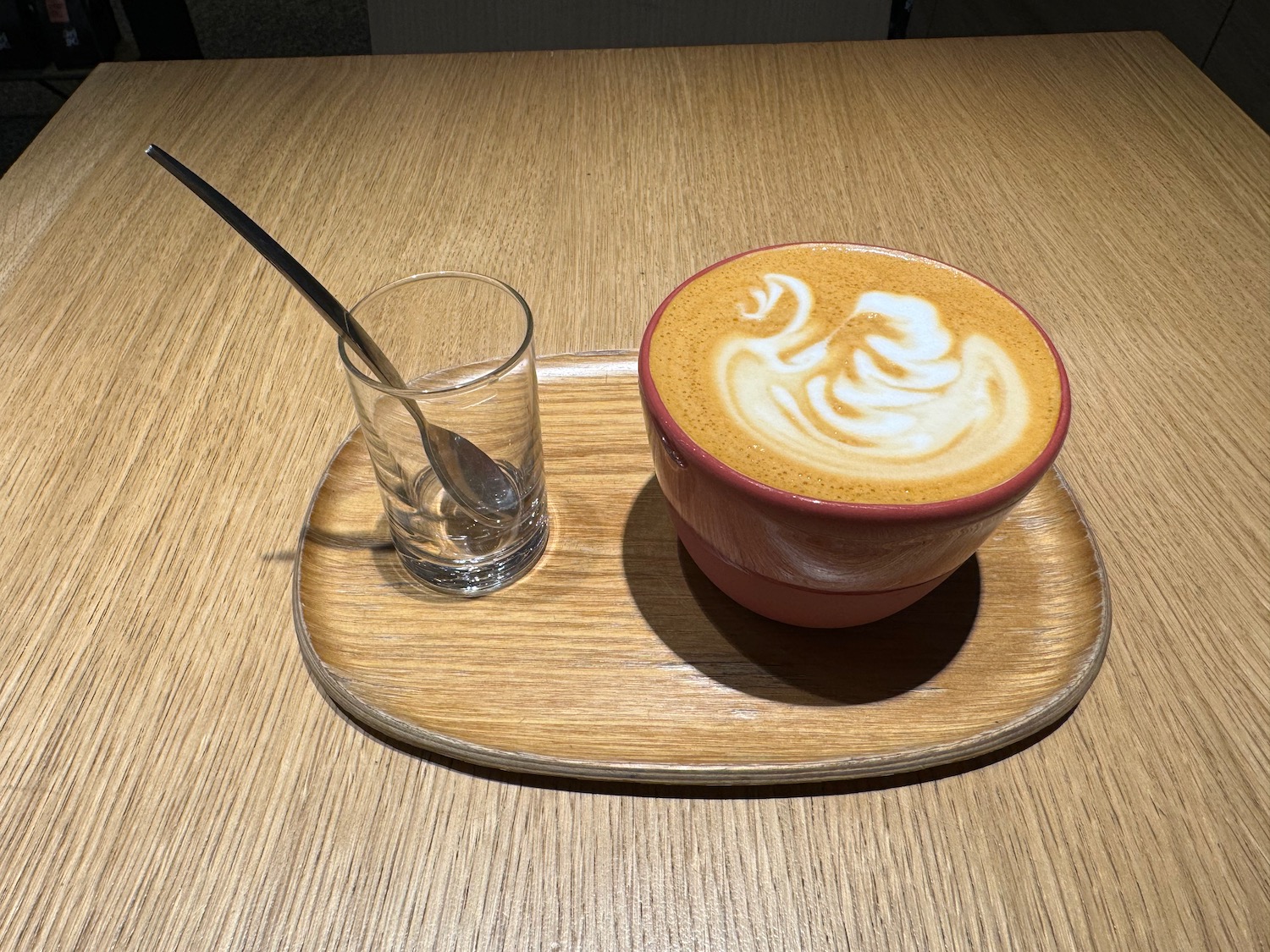 O ceașcă de cafea cu o lingură și un pahar pe o farfurie de lemn
