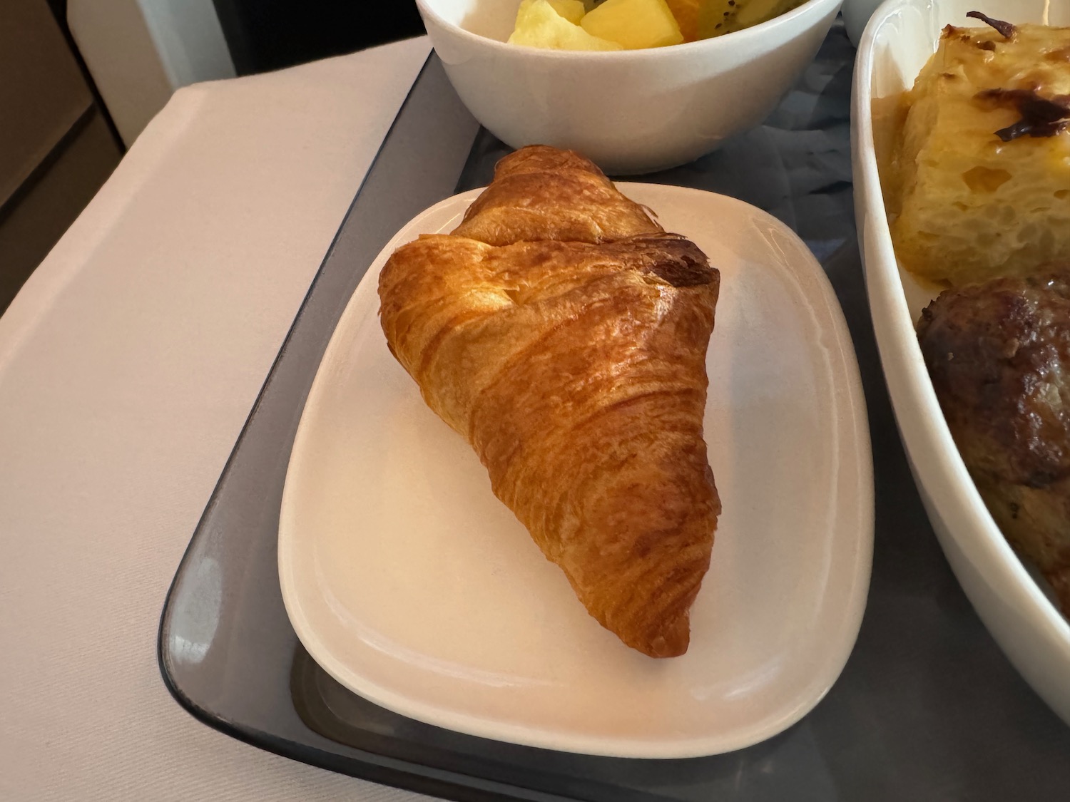 a croissant on a plate next to a bowl of fruit