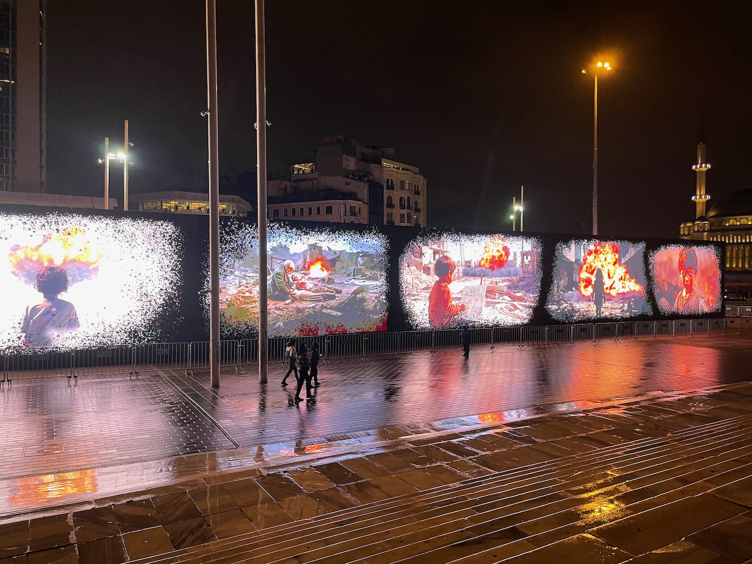 a group of people walking on a wet sidewalk with large screens