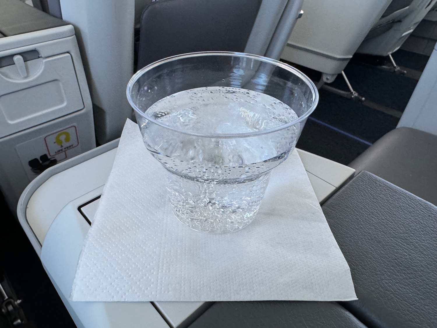 a clear plastic cup with ice on a napkin on a seat