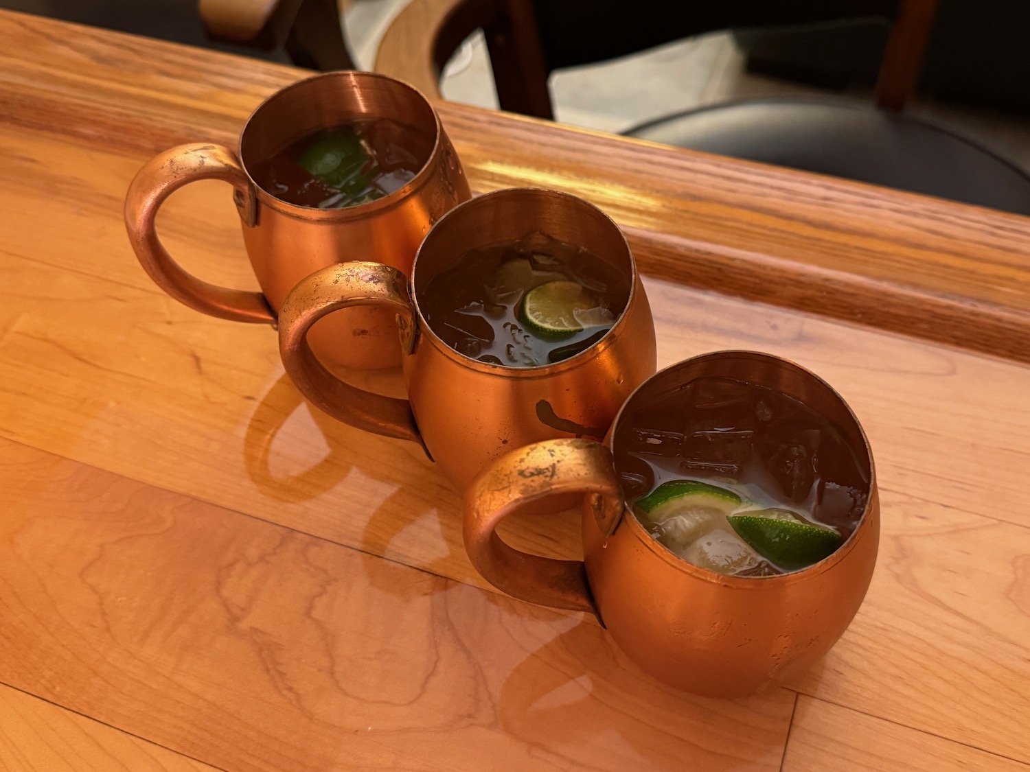a group of copper mugs with liquid and limes on a wood surface