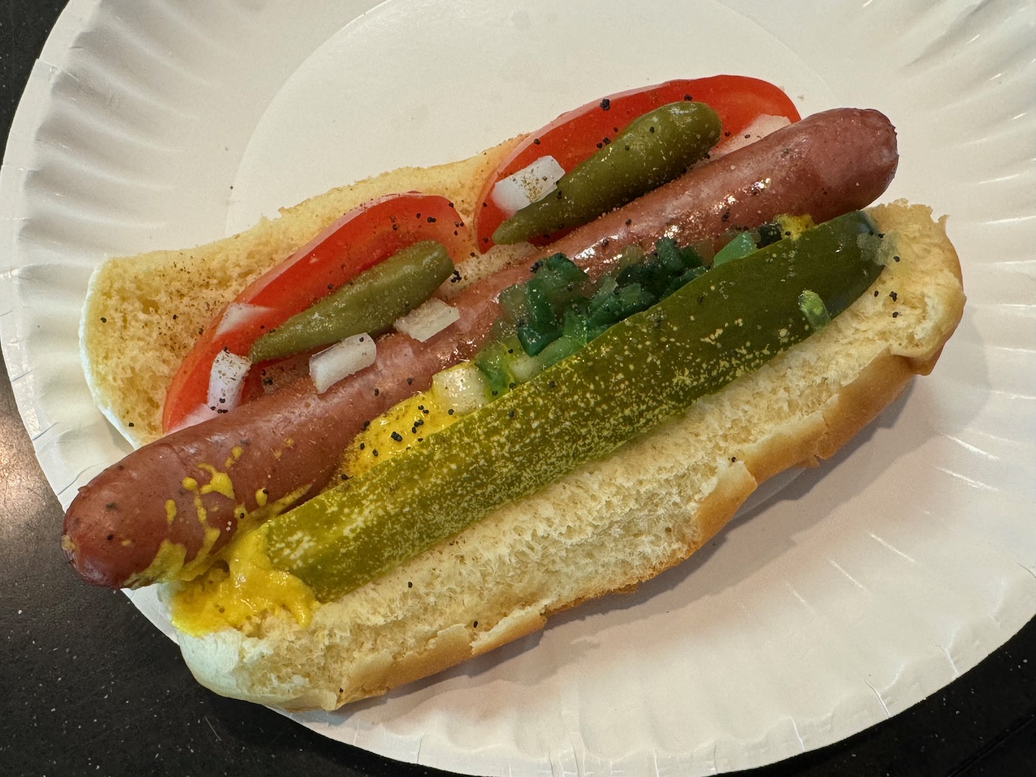 a hot dog with pickles and mustard on a paper plate