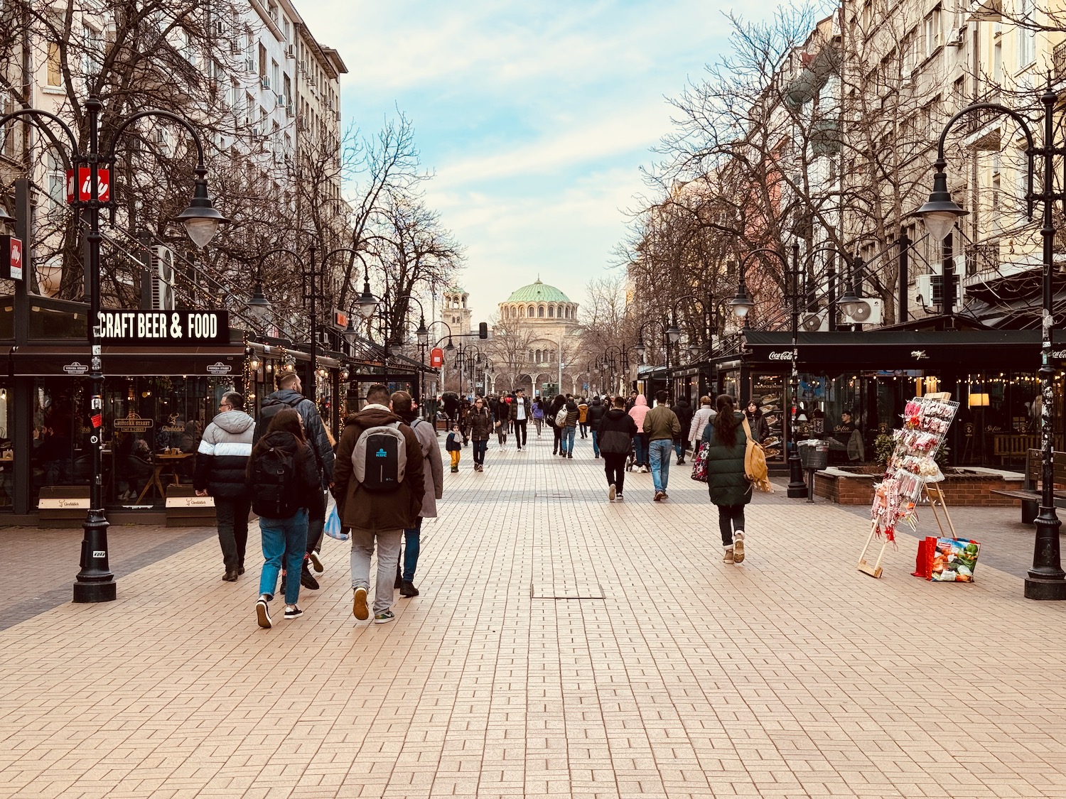 a group of people walking on a brick sidewalk with La Rambla, Barcelona in the background