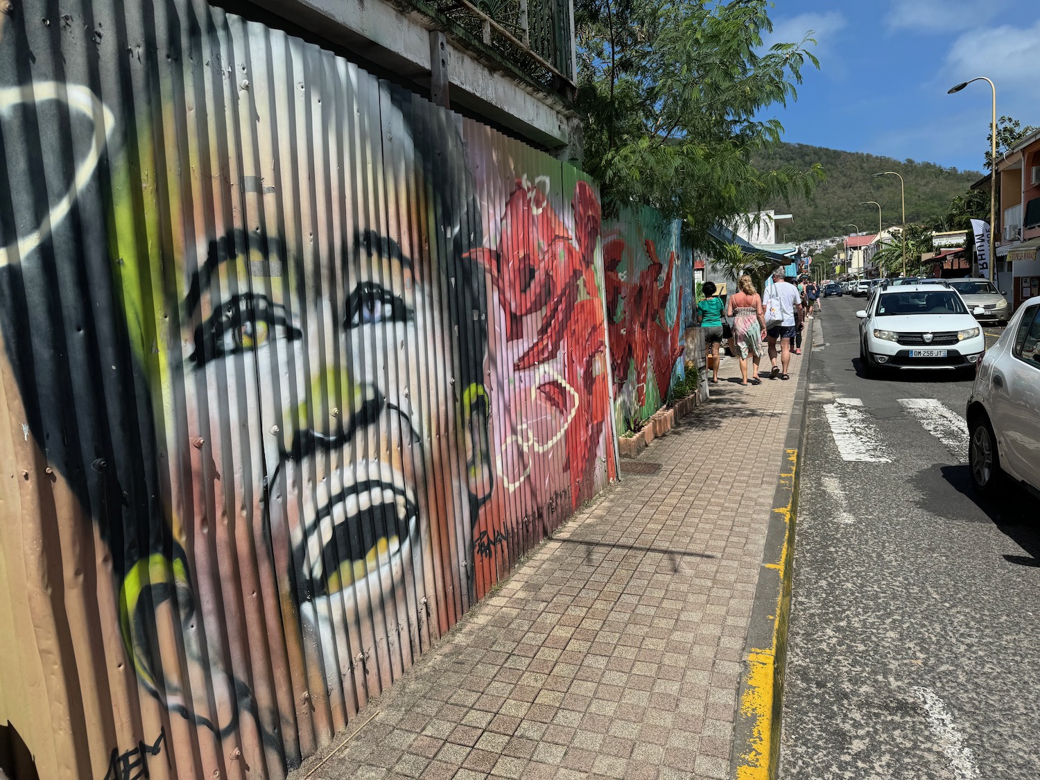 a group of people walking on a sidewalk next to a wall with graffiti