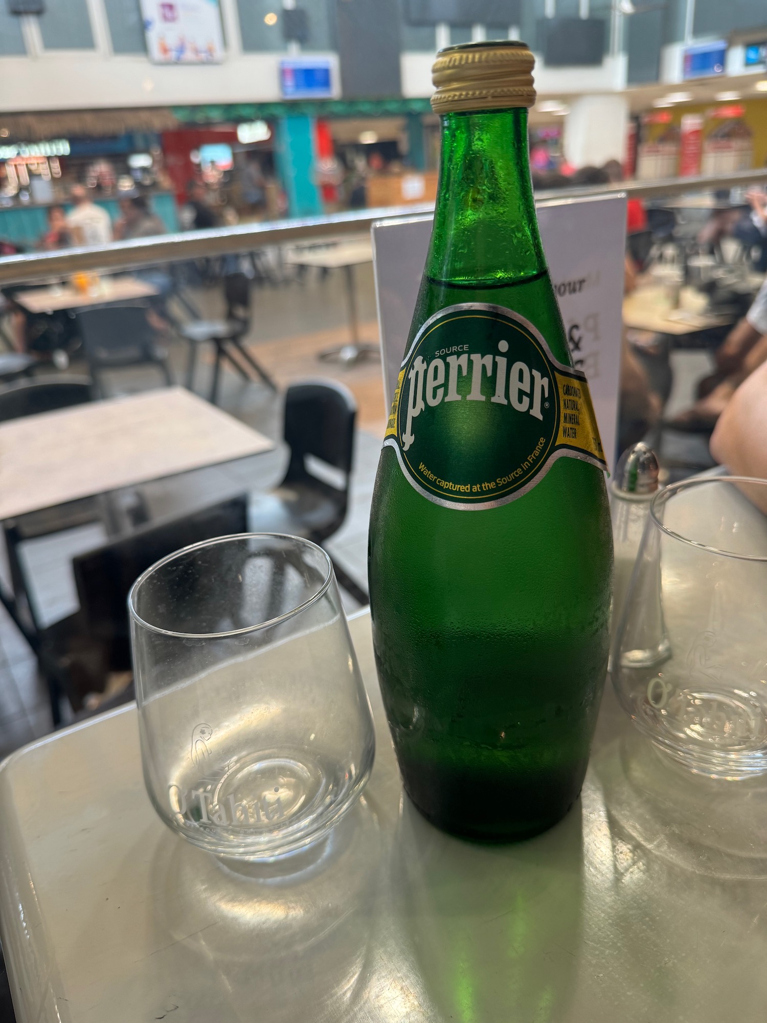 a bottle of sparkling water and empty glasses on a table