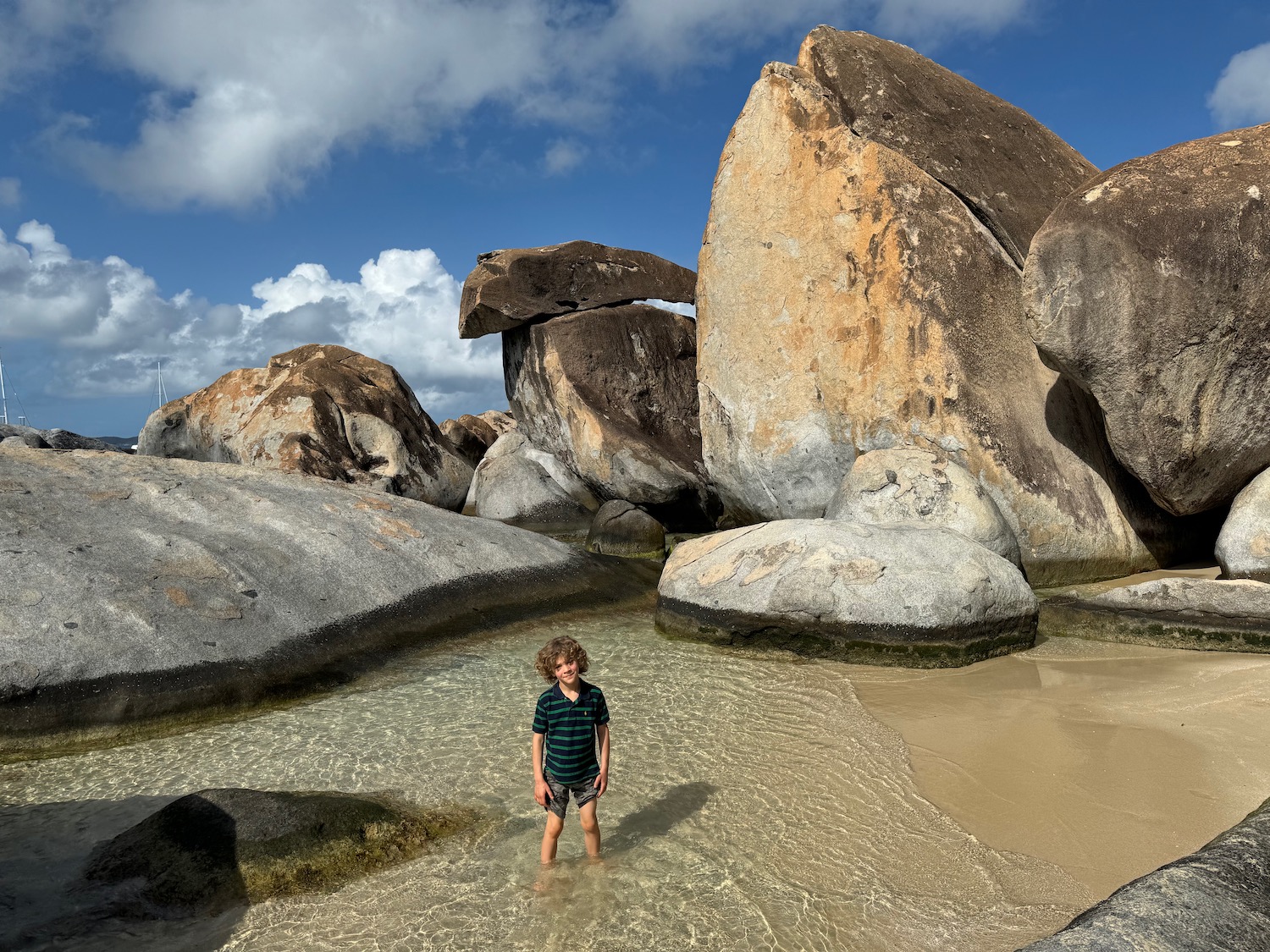 a boy standing in water with large rocks in the background