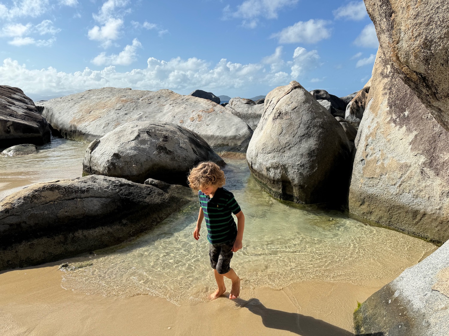a boy standing on a beach with large rocks