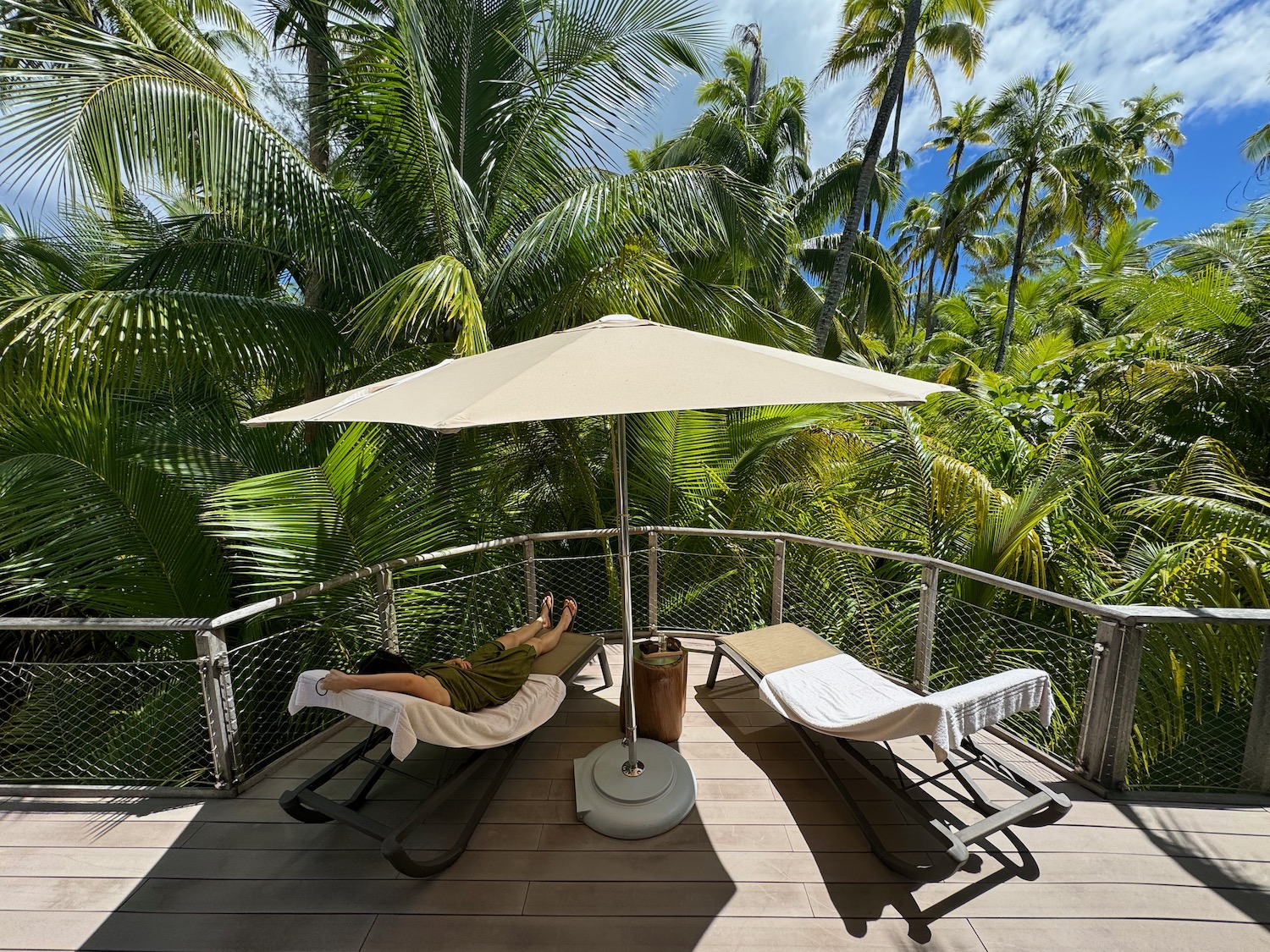 a person lying on a deck with a umbrella and palm trees