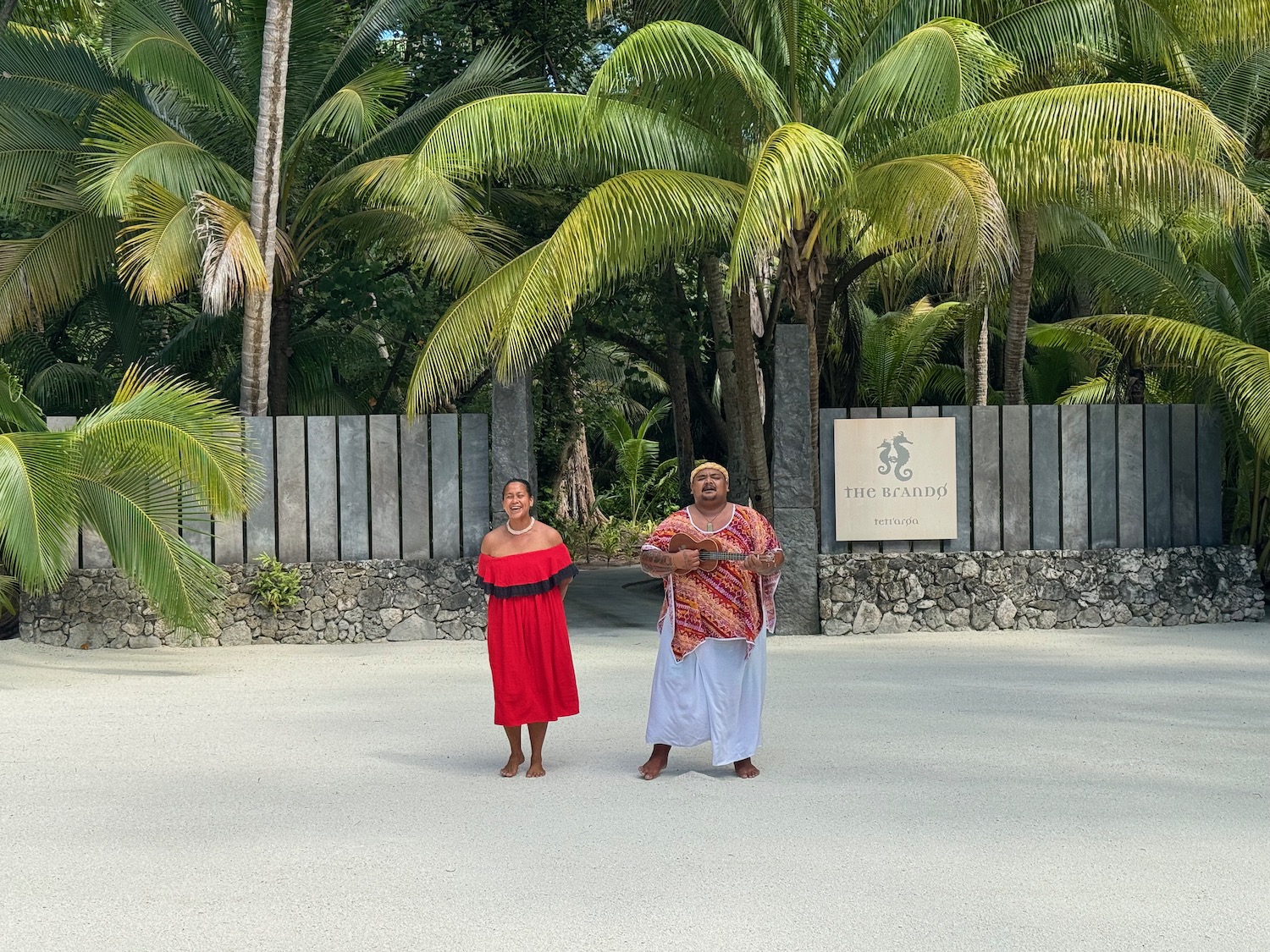 a man and woman standing in a dirt area with palm trees