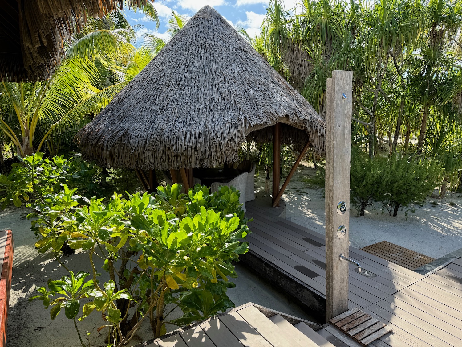 a hut with a thatched roof and a wooden deck in the middle of a tropical beach