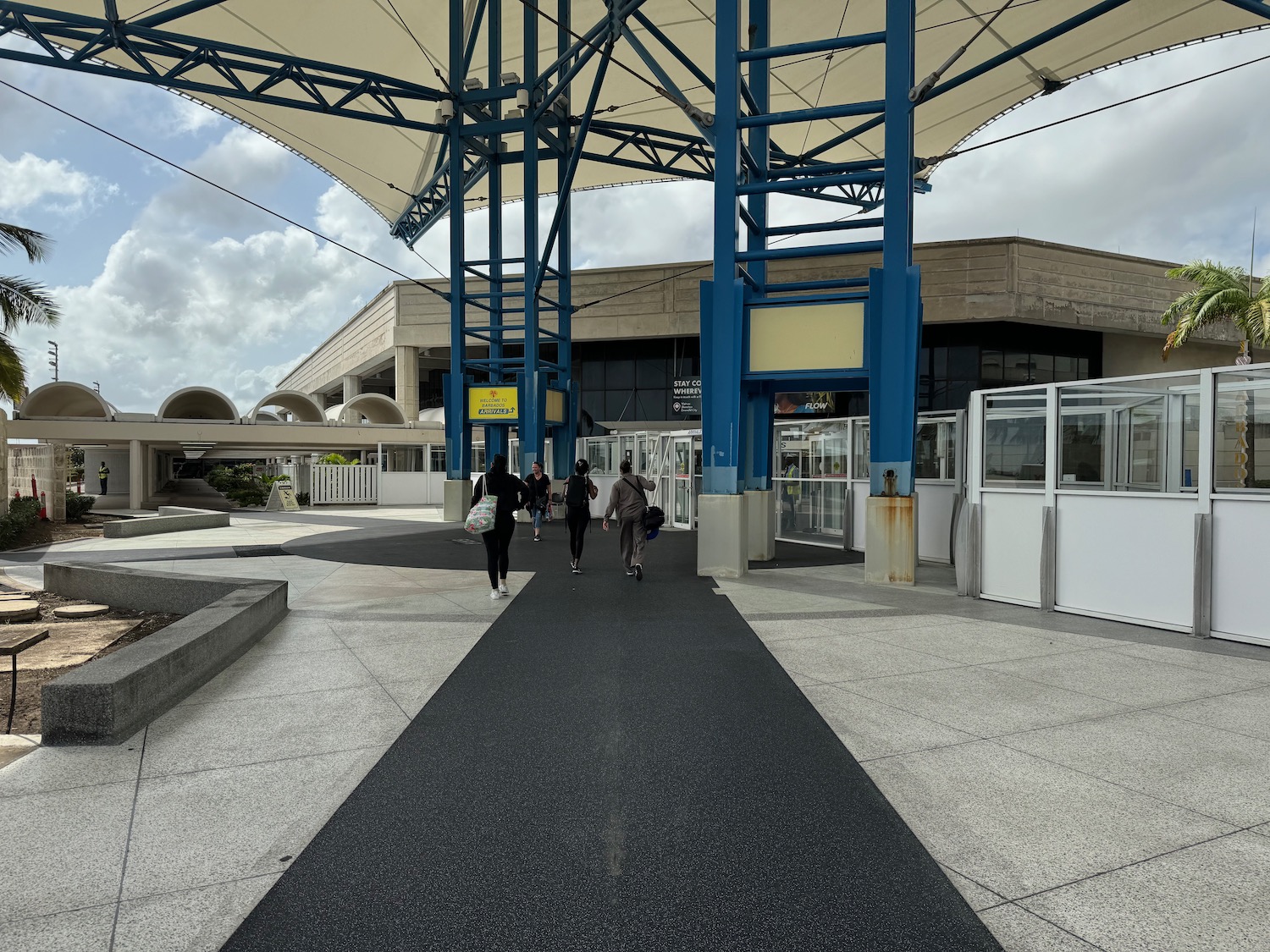 people walking on a walkway with blue pillars and a building