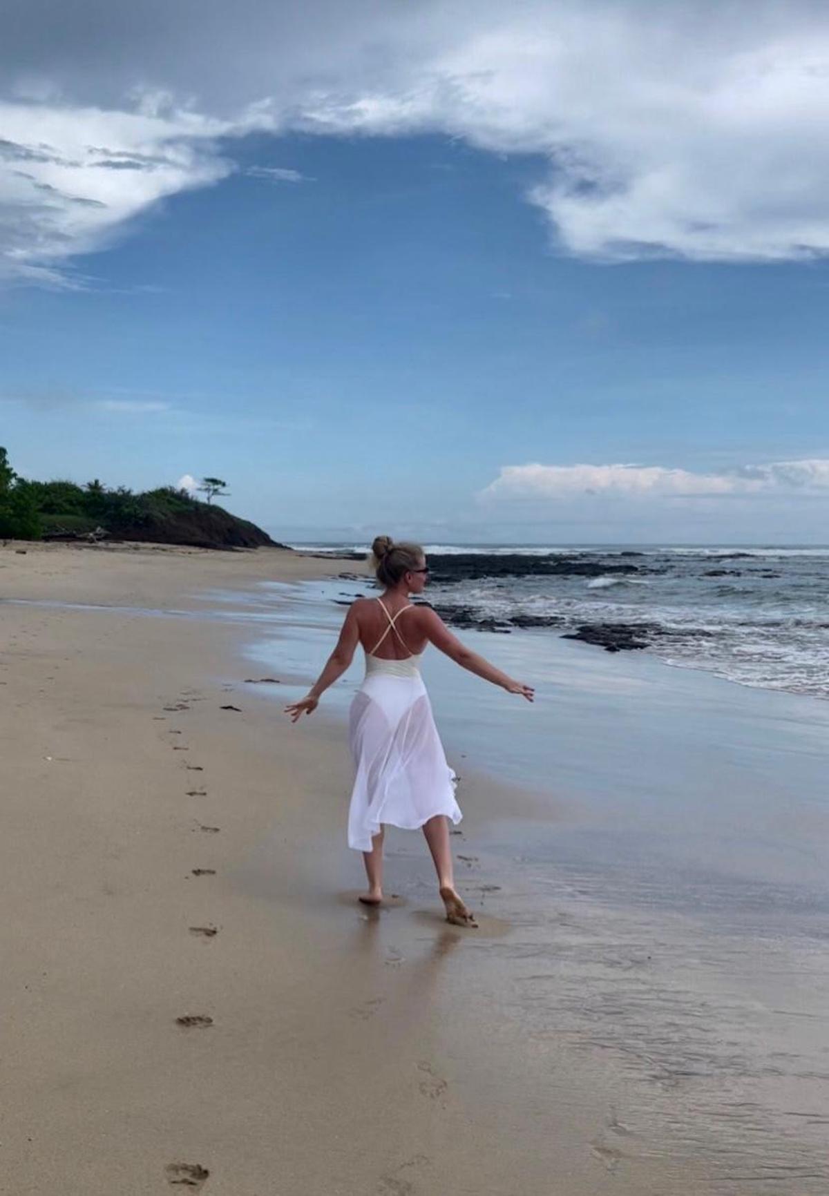 a woman in a white dress walking on a beach