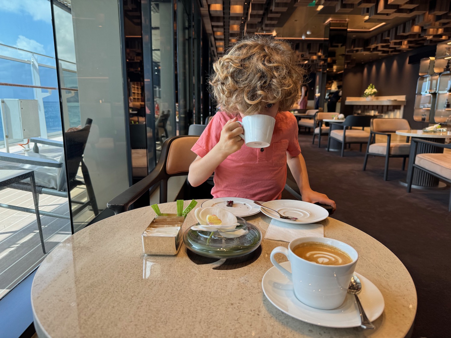 a child sitting at a table with a cup of coffee