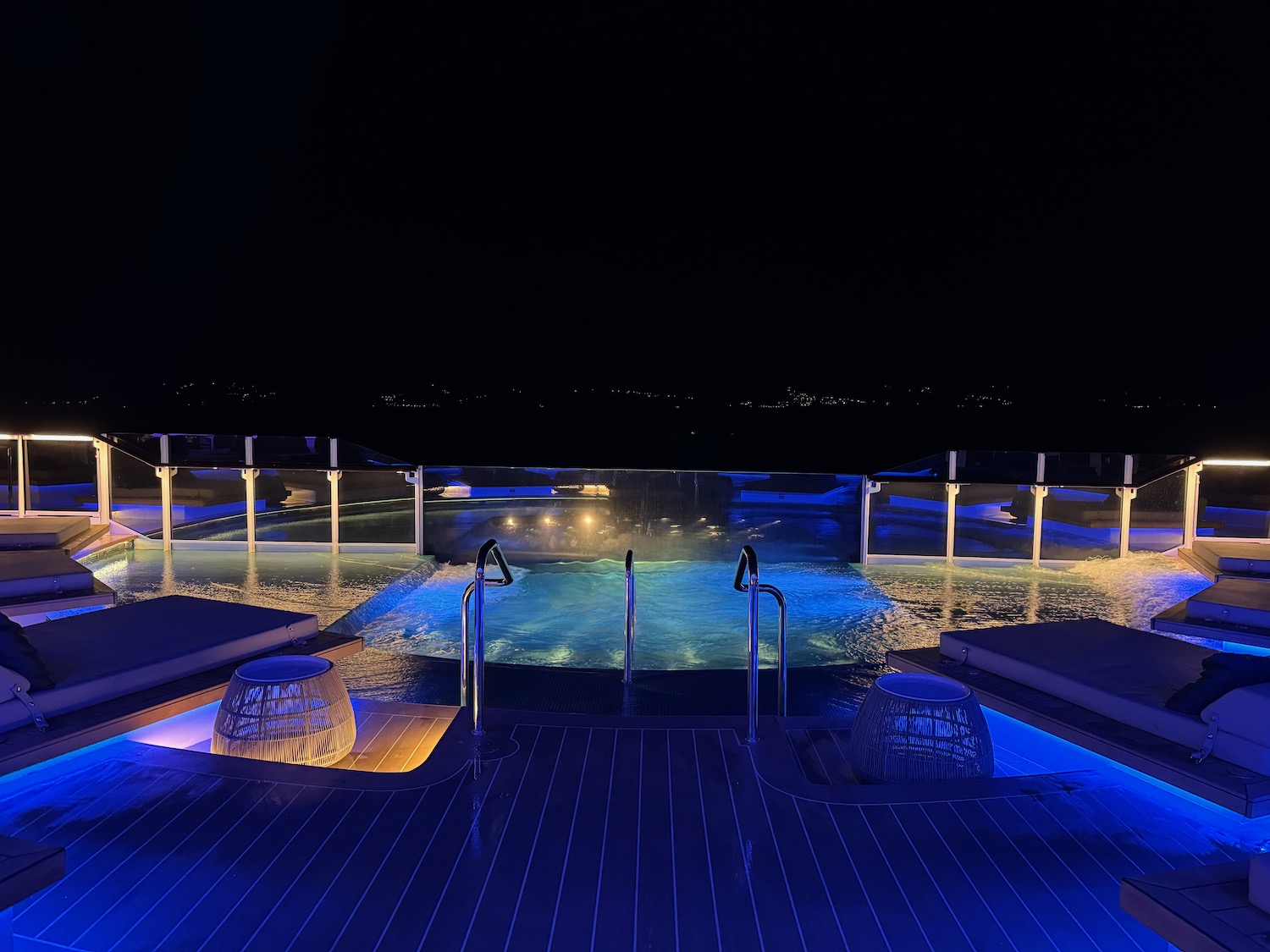 a pool with a deck and chairs at night