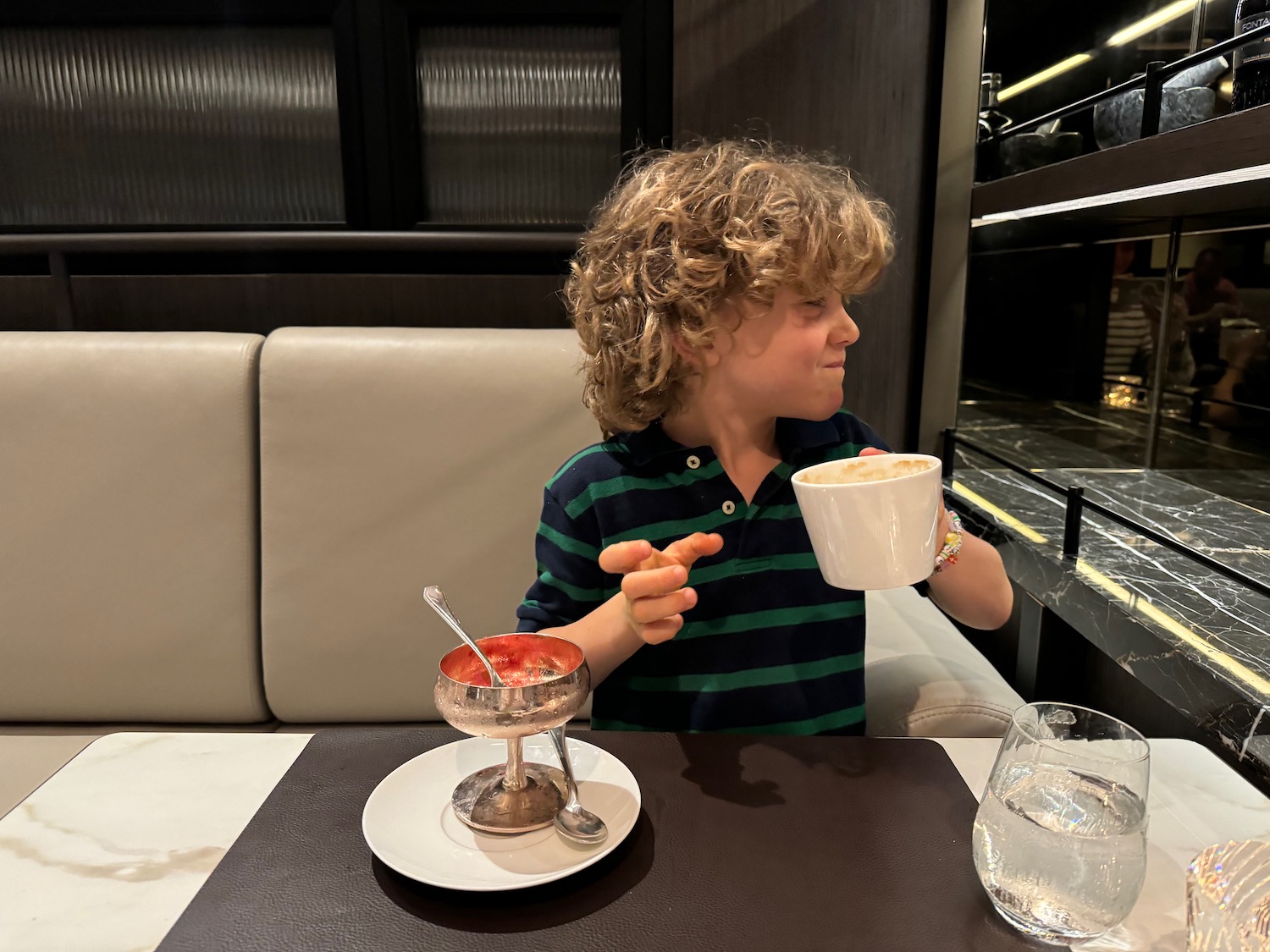 a boy sitting at a table with a cup of soup