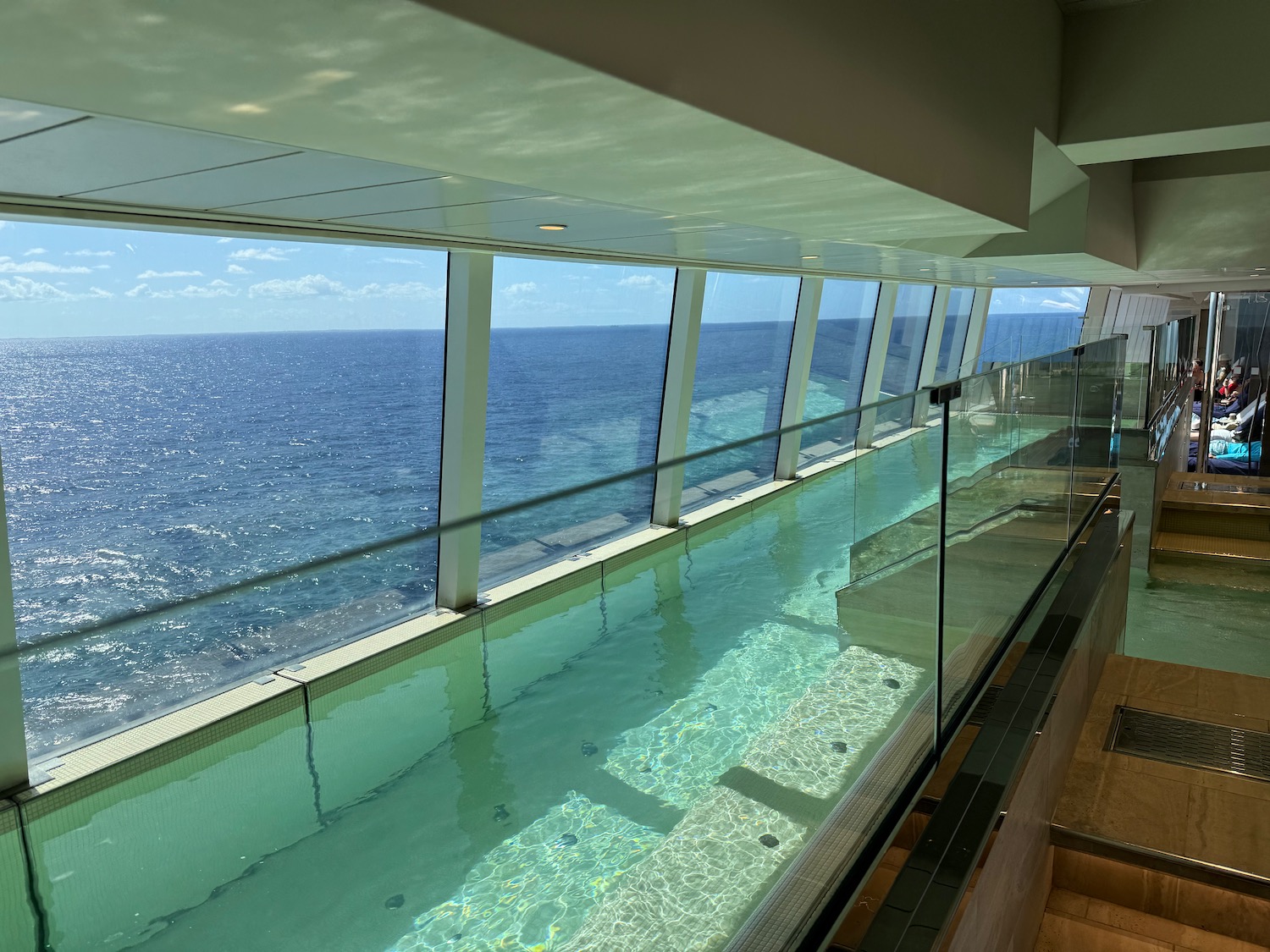 a pool with a glass wall and a staircase overlooking the ocean