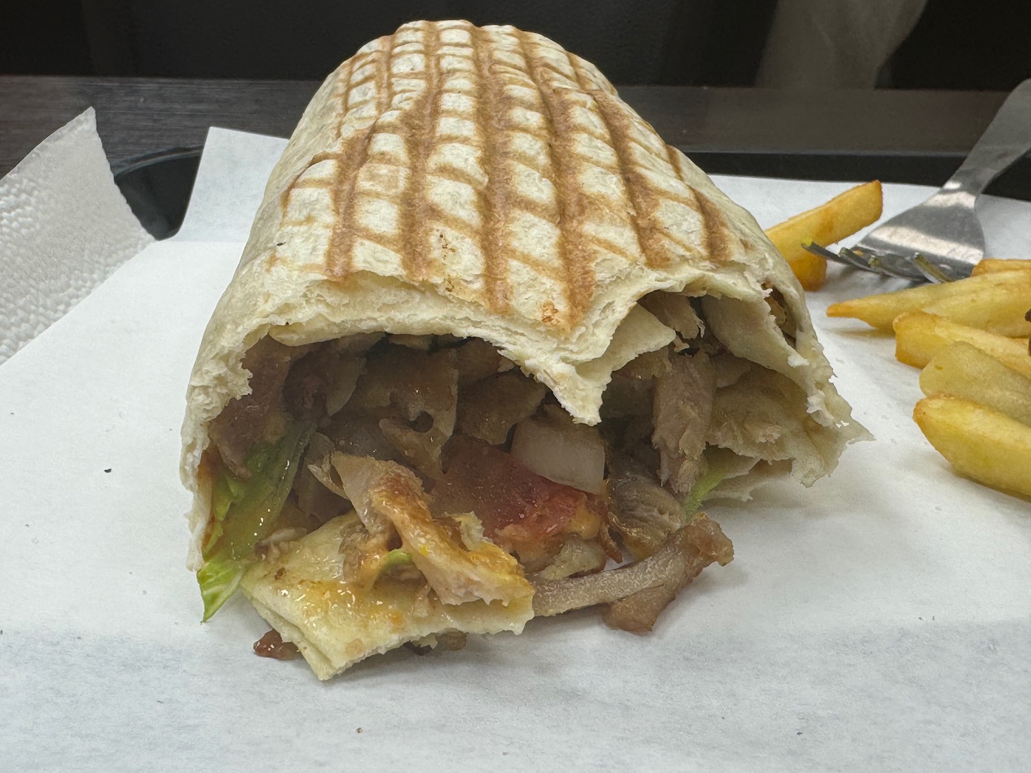 a burrito with meat and vegetables on a white paper